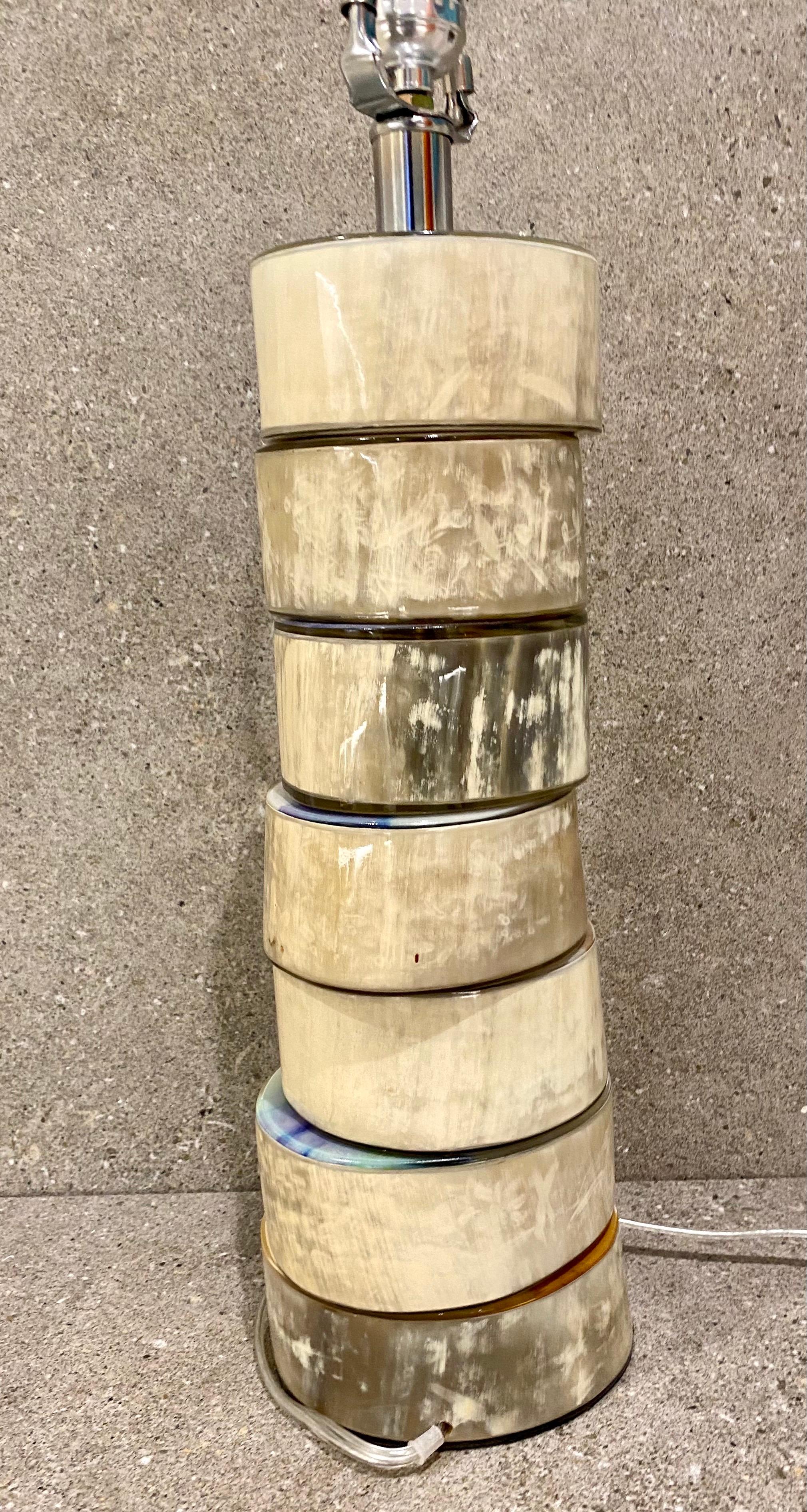 A Stylish stacked buffalo horn table lamp by Jamie Young. The base is a stack of disks made of genuine polished buffalo horn. Each disk has a narrow metal flange and is slightly off-set from its neighbor. The lamp powered on and off switch.