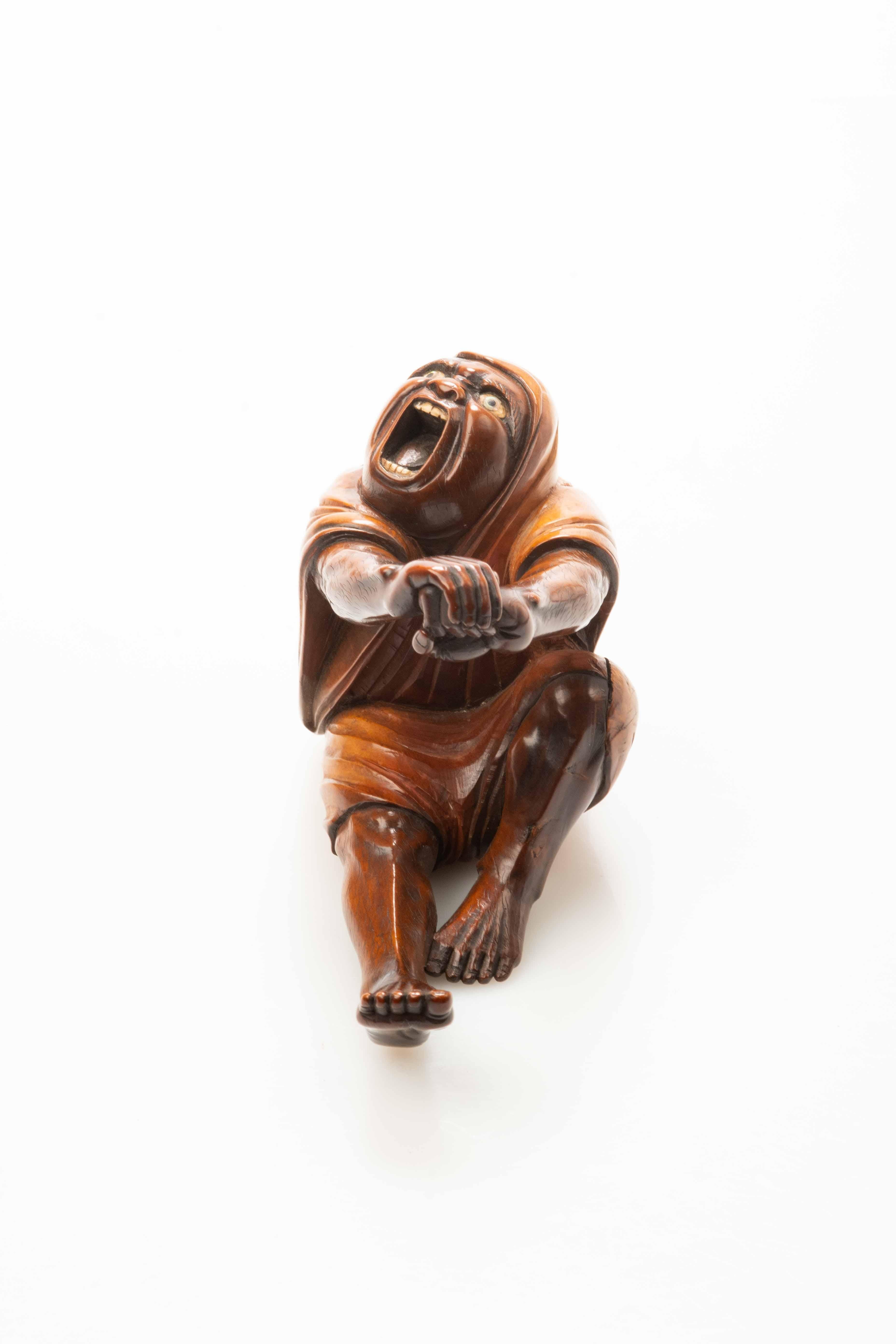 Boxwood okimono with horn and mother of pearl, portraying the moment of Daruma's awakening. The figure, sitting and stretching, has wide eyes and an open mouth.

Under the base, the signature “Tomokata” is engraved on red lacquer.

Origin: