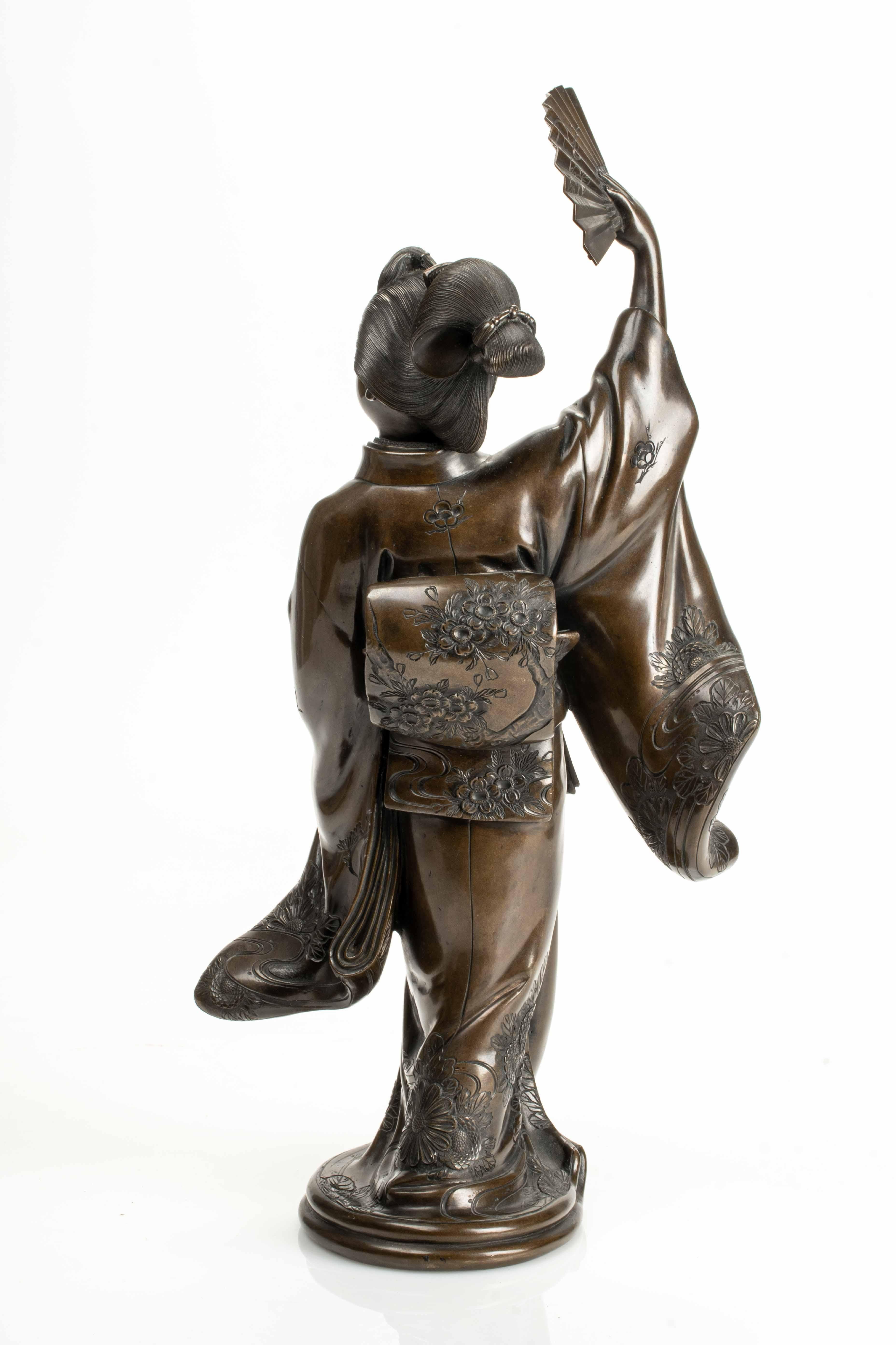 A Japanese okimono bronze (sculpture) depicting a dancer holding a fan, inspired by the Nihon Buyō classical dance tradition.

The long kimono and wide obi are adorned with floral motifs and feature finely chiseled details.

Signed under the base