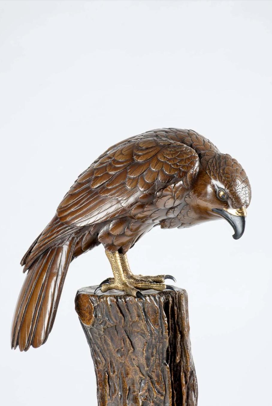 A Japanese bronze sculpture depicting a perched falcon in light patina with polychrome eyes, beak and legs in black contrasting with pure gold.

The sculpture depicts the falcon in a moment of serene repose, perched with an aura of regal