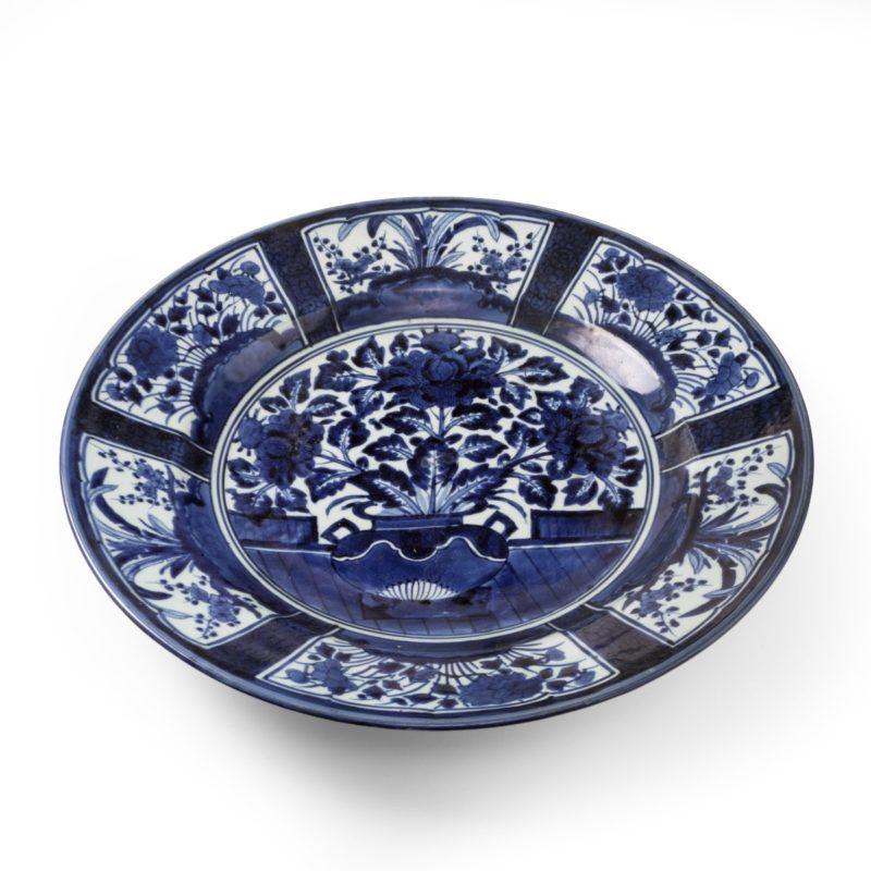 Grand chargeur de forme circulaire d'Arita, peint en bleu cobalt sous une épaisse glaçure brillante, avec un vase central de fleurs de pivoines sur une plate-forme, le bord évasé avec des panneaux de motifs floraux alternés. Circa 1700.

Une fois