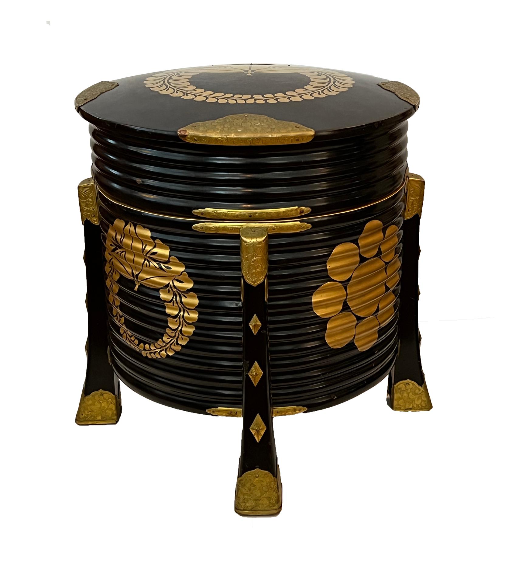 this large ribbed and cylindrical Japanese shell-game box with domed lid decorated overall with Maki-e (gold lacquered) foliate wreaths and stylized flower heads and incised brass mounts; raised on four splayed supports.
Hokai boxes became prominent