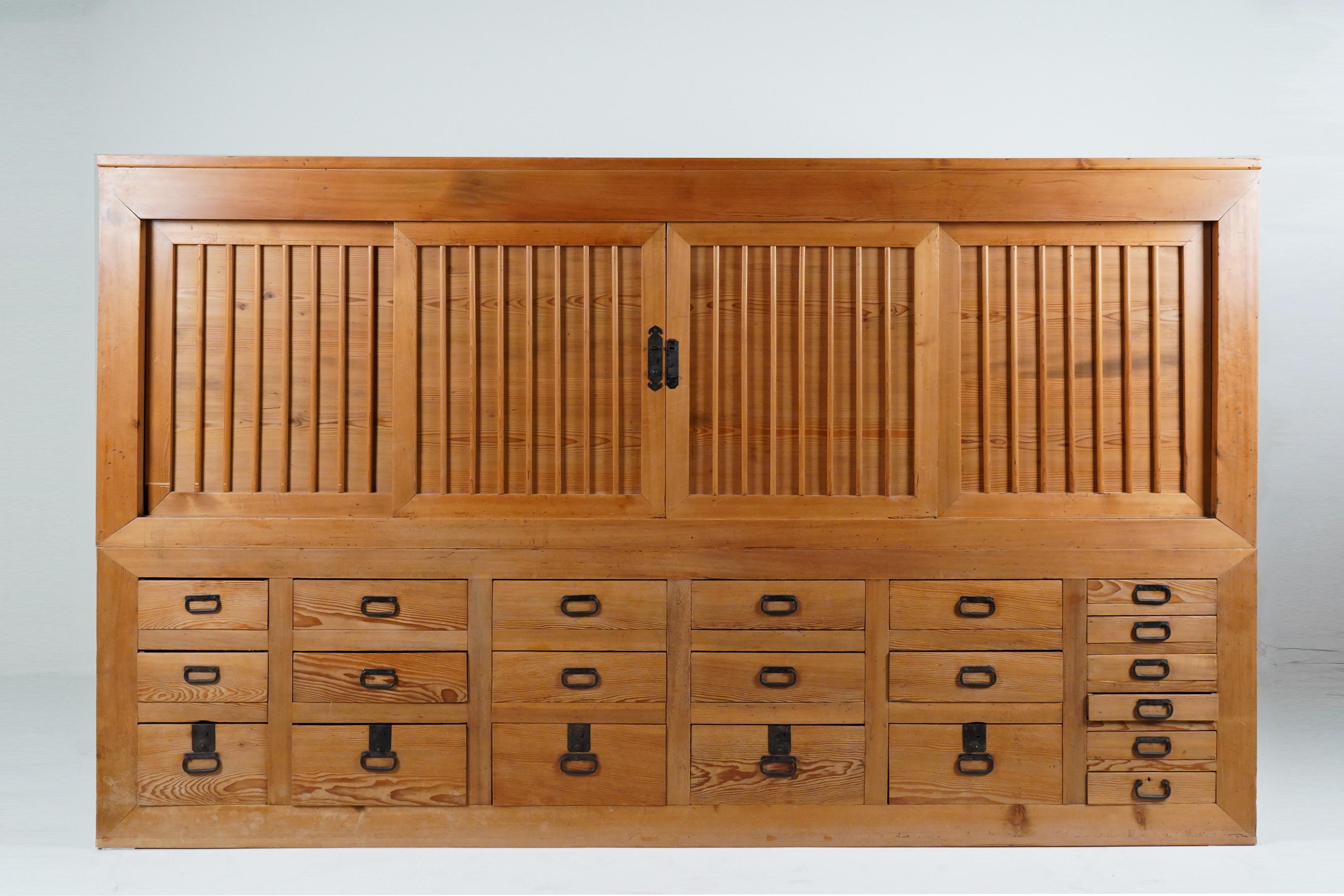 A large 2-piece Japanese Mizuya kitchen tansu with 21 drawers and an upper cabinet with 4 sliding doors. Behind the sliding doors is a large open space bisected by a half-depth shelf. The exterior has been totally stripped of its original lacquer