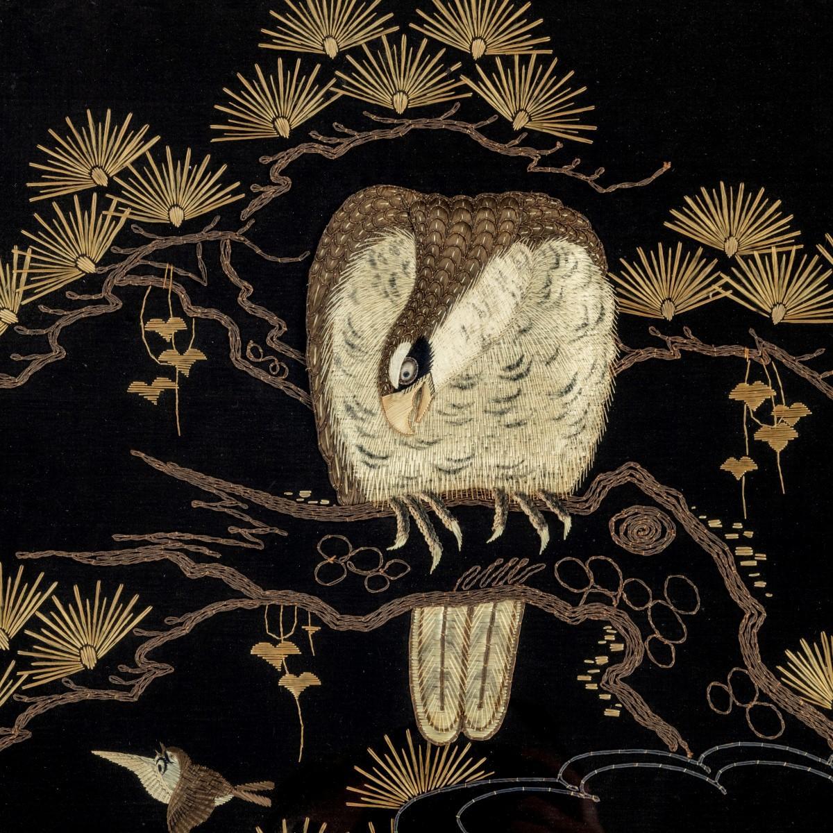 A Japanese needlework of an eagle, worked in gold, silver and grey silks on a dark ground with the large bird perched on a pine branch watching a sparrow flying past, inscribed on the reverse ‘This picture given to Muriel Putnam-Smith July 1999 by