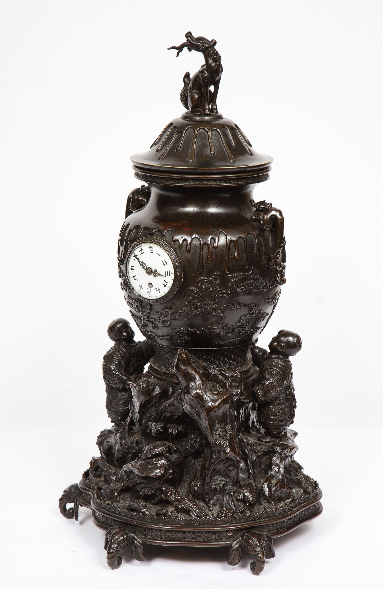 A Japanese patinated bronze figural clock vase, Meiji period, in the Japonisme taste.

Depicting two young Japanese boys holding an urn, surrounded by hills, mountains and nature, on elephant head feet. Very interesting and unusual
