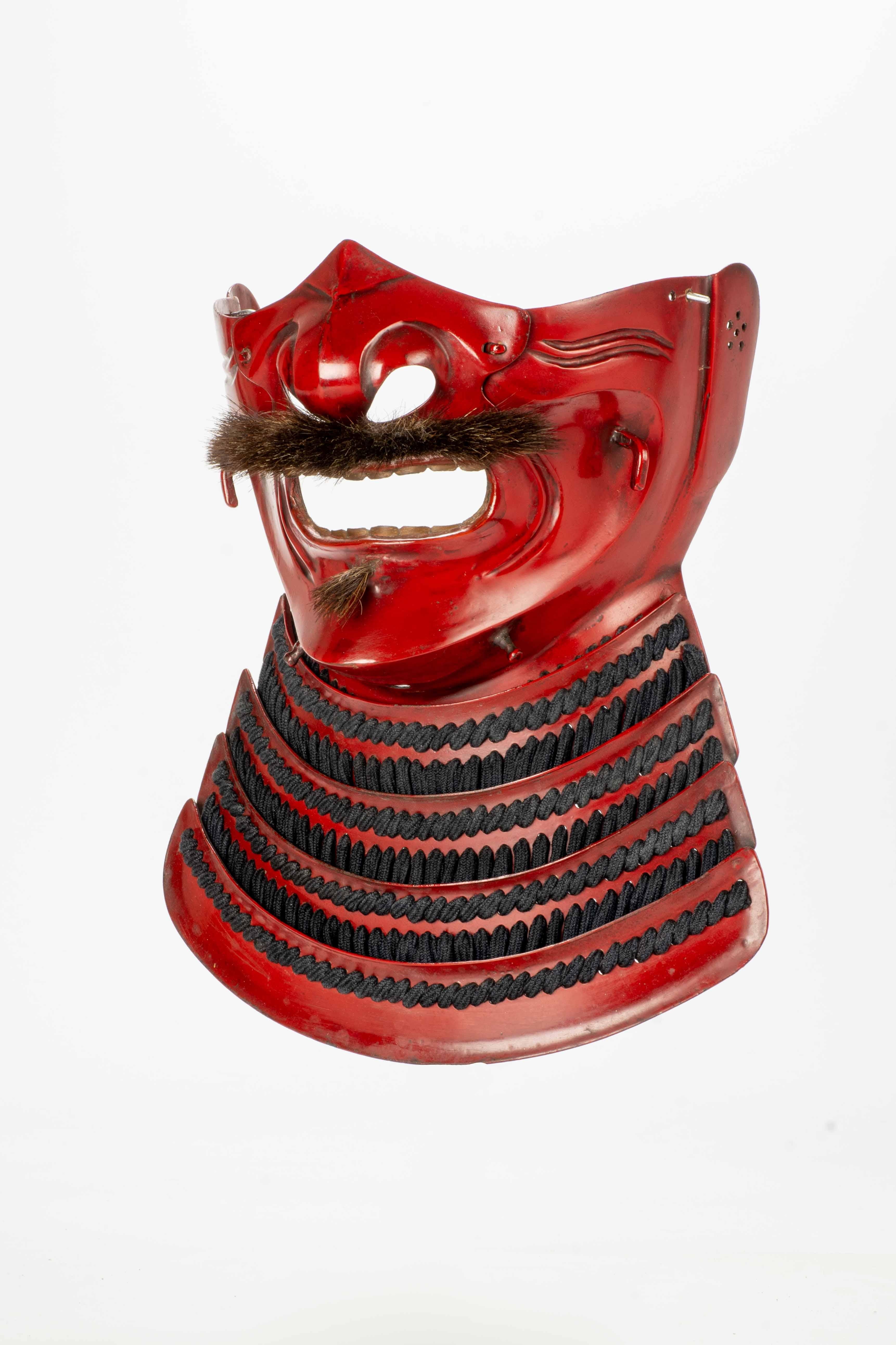 Samurai menpo mask with the 'fierce' ressei expression, with the iron and red lacquer surface which gives the face deep and marked wrinkles.

The generously sized nose adds a distinctive element to the face of the mask, together with the brush