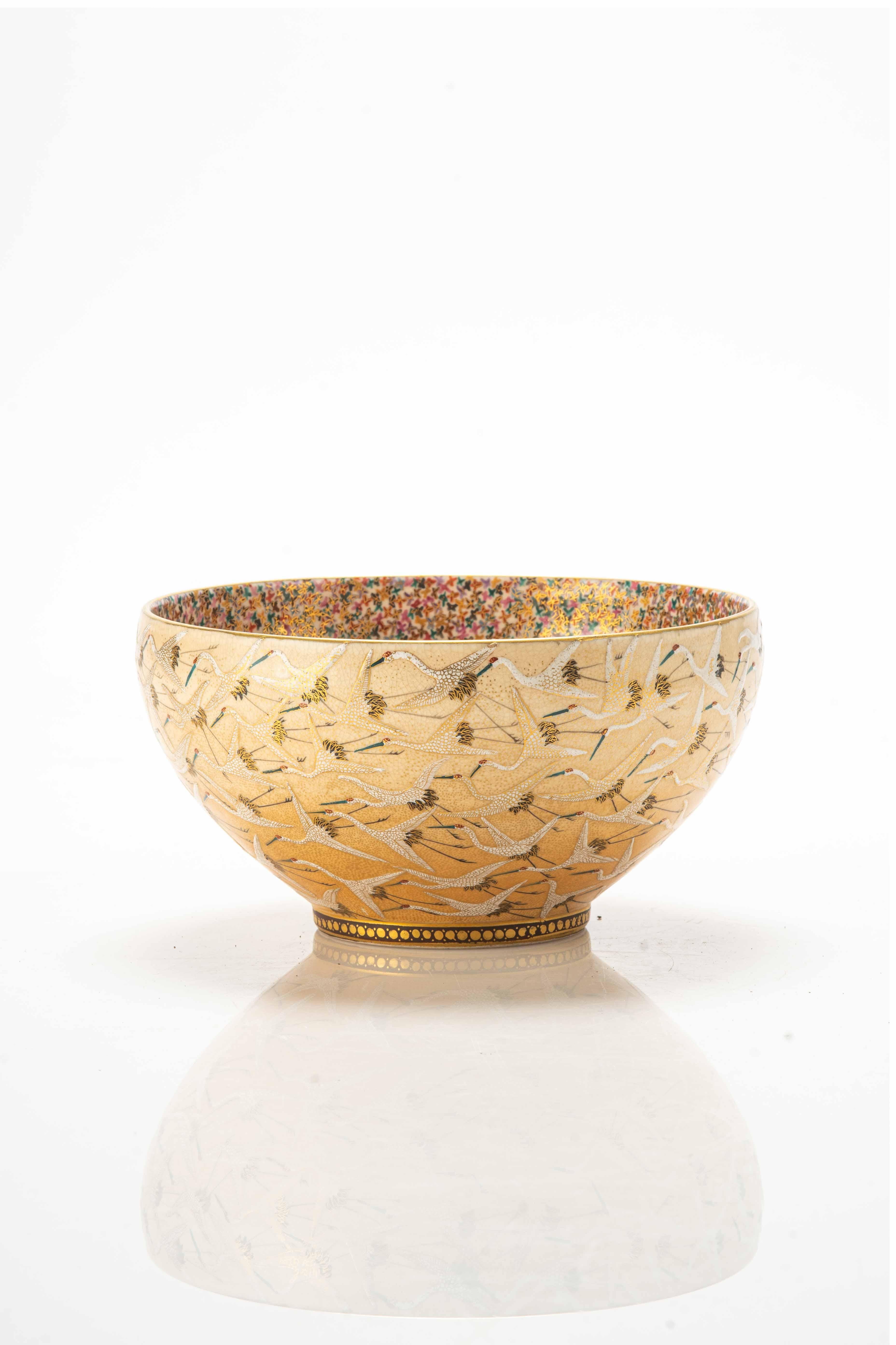 Schale aus Satsuma-Keramik mit Reliefglasuren und goldenen Details, die ein Motiv von Mandschurenkranichen im Flug zeigen, die in der japanischen Kultur Symbole für Langlebigkeit und Glück sind.

Das Innere der Schale zeigt ein dichtes Motiv von