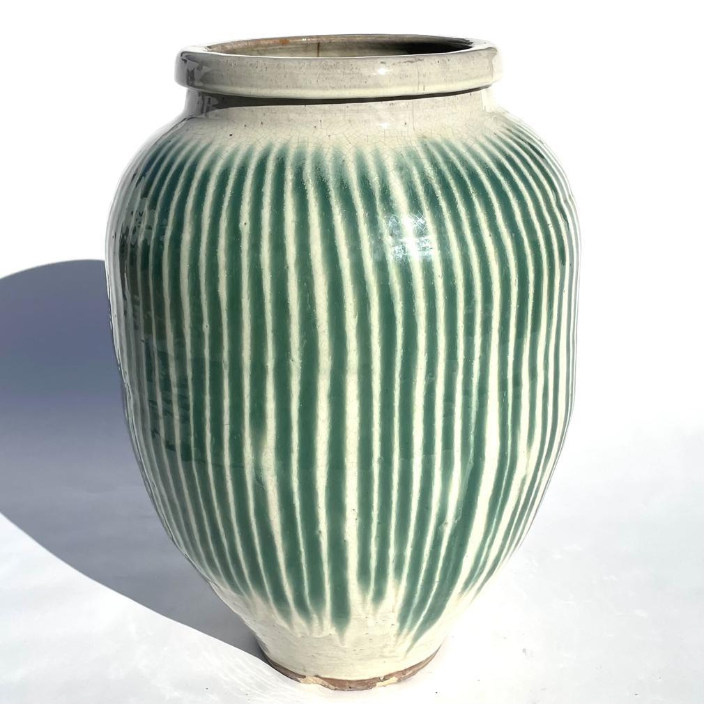 The large stoneware pot glazed with vertical green stripes on an off-white background in a watermelon-style crackled glaze pattern. The interior glazed brown. the form of wide body , tapering to a narrow flat bottomed base and the mouth narrow above