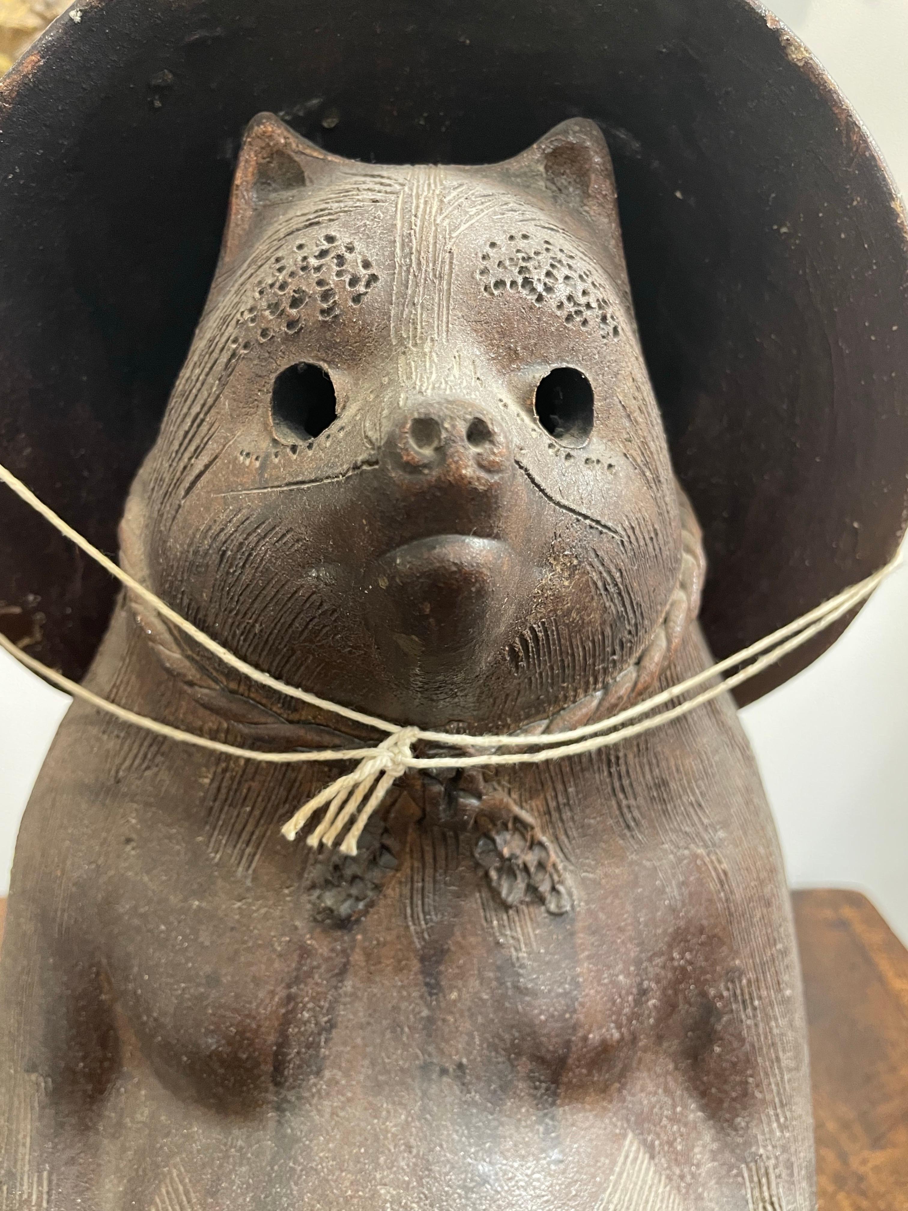A Japanese Tanuki, Early 20th Century

Provenance:  
Private South Australian Collection. 

Description:
The rotund ceramic Tanuki depicted in typical fashion, with large testes and a straw hat, carrying a promissory note in his left hand, the right