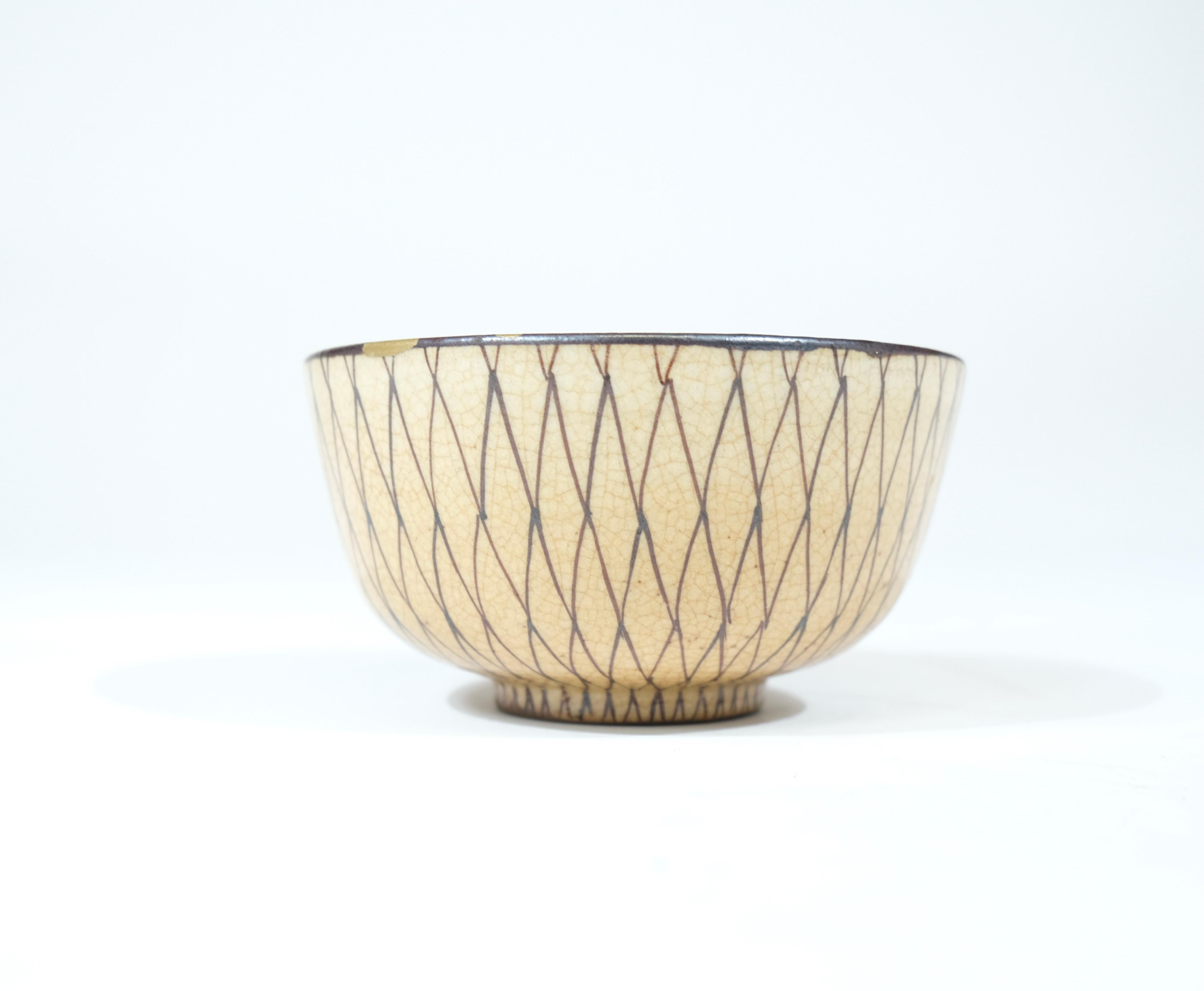 A charming Japanese tea bowl glazed in beige color with a pattern of a net on top. On the rim it has a few chips that have been overpainted with gilt color.