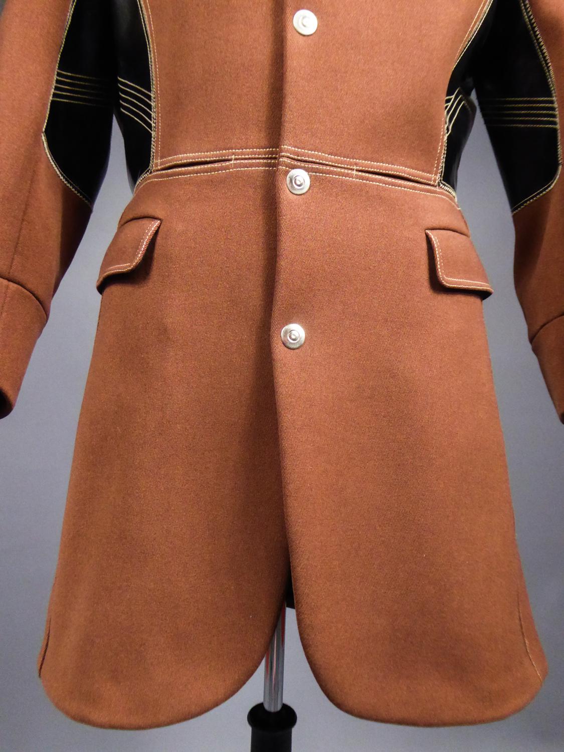 Circa 1990/2000

France

Ample masculine coat signed Jean-Paul Gaultier in thick twill of light brown wool dating from the 1990s. Long-tailed frock coat cut, split back and small officer collar in black velvet. Black vinyl panels on the sides, and
