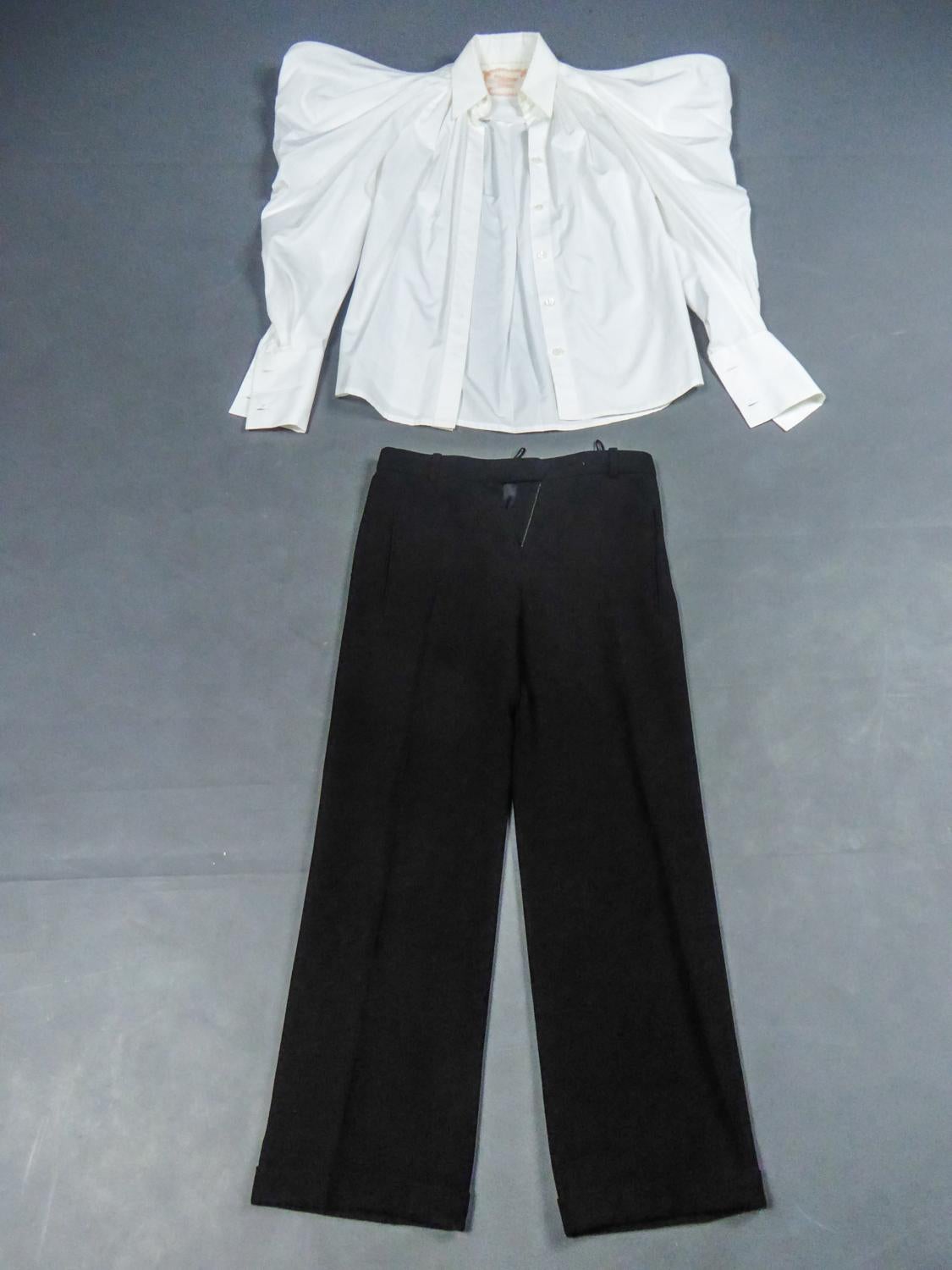Spring Summer Collection 2014
Frankreich

Haute Couture Set bestehend aus einer Bluse in weißer Baumwollpopeline mit Puffärmeln und einer Hose in schwarzem Krepp aus der Frühjahr-Sommer-Kollektion 2014 Passage n ° 9 Jean Paul Gaultier. Bluse mit