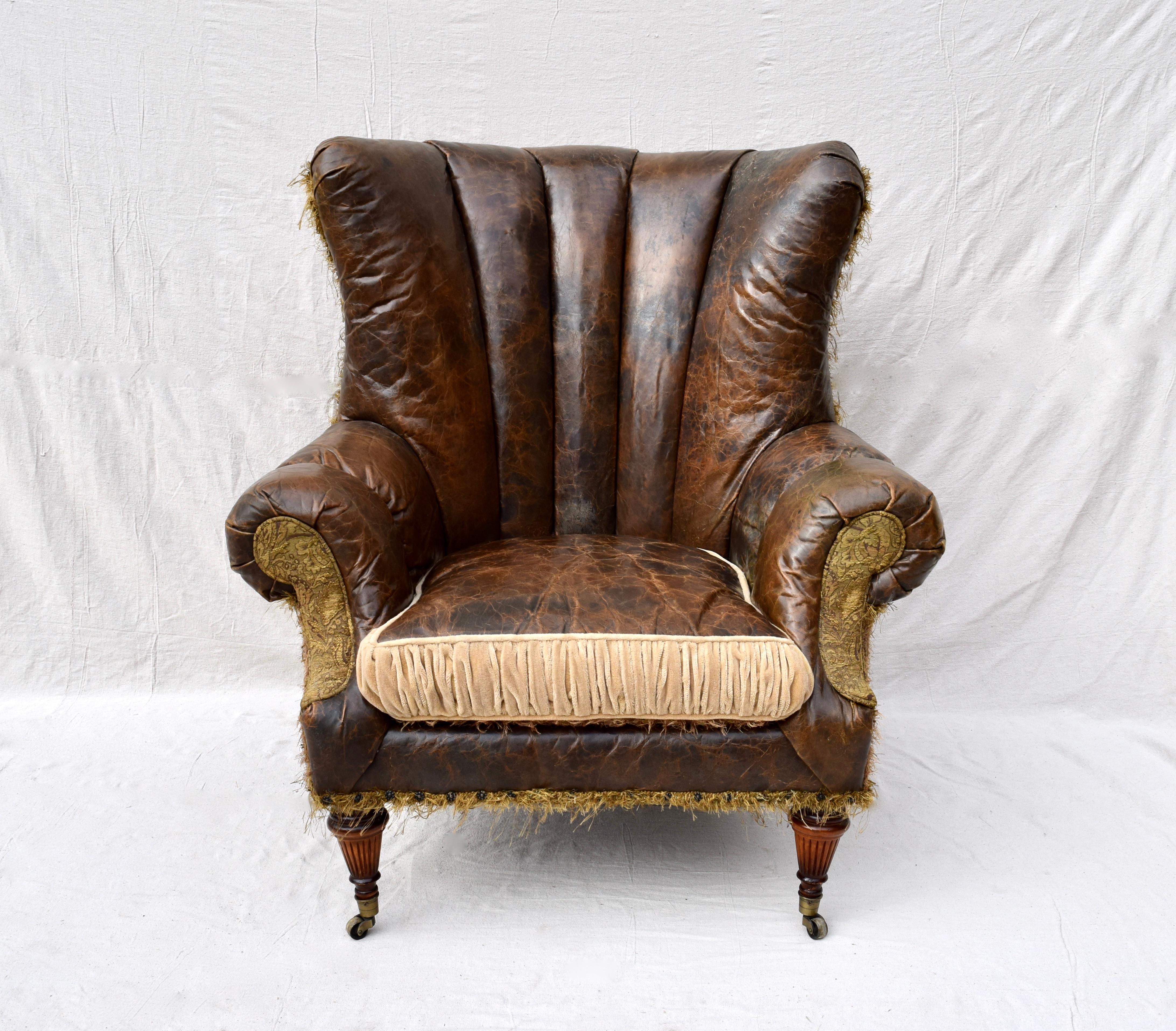 A signed Jeff Zimmerman wingback chair and matching ottoman, both upholstered in distressed leather and plush Mohair, decorated with brass nail heads. Features include goose down filled reversible loose seat cushion, with velcro-attached ottoman