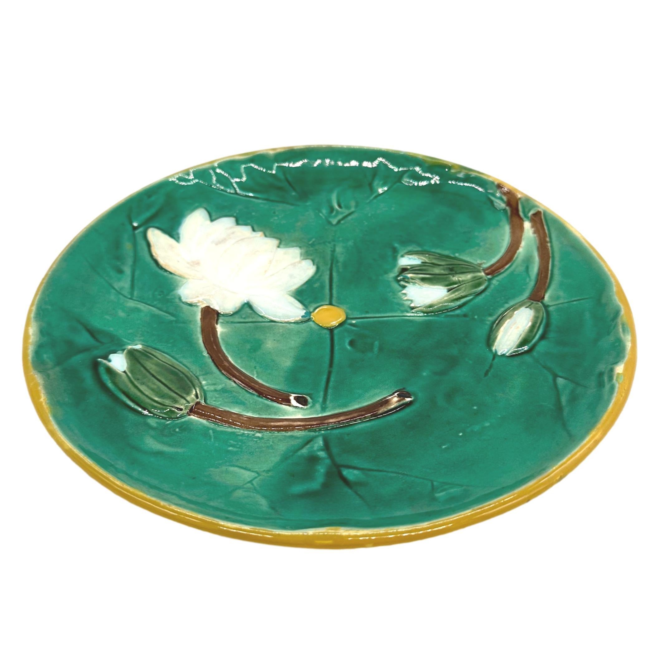 Joseph Holdcroft Majolica Pond Lily Plate, glazed in greens, and molded with flowering white lilies, with a yellow button to the center and bordered in yellow, the reverse with mottled glazing and impressed 'JH' monogram within a circle. 
BOOK