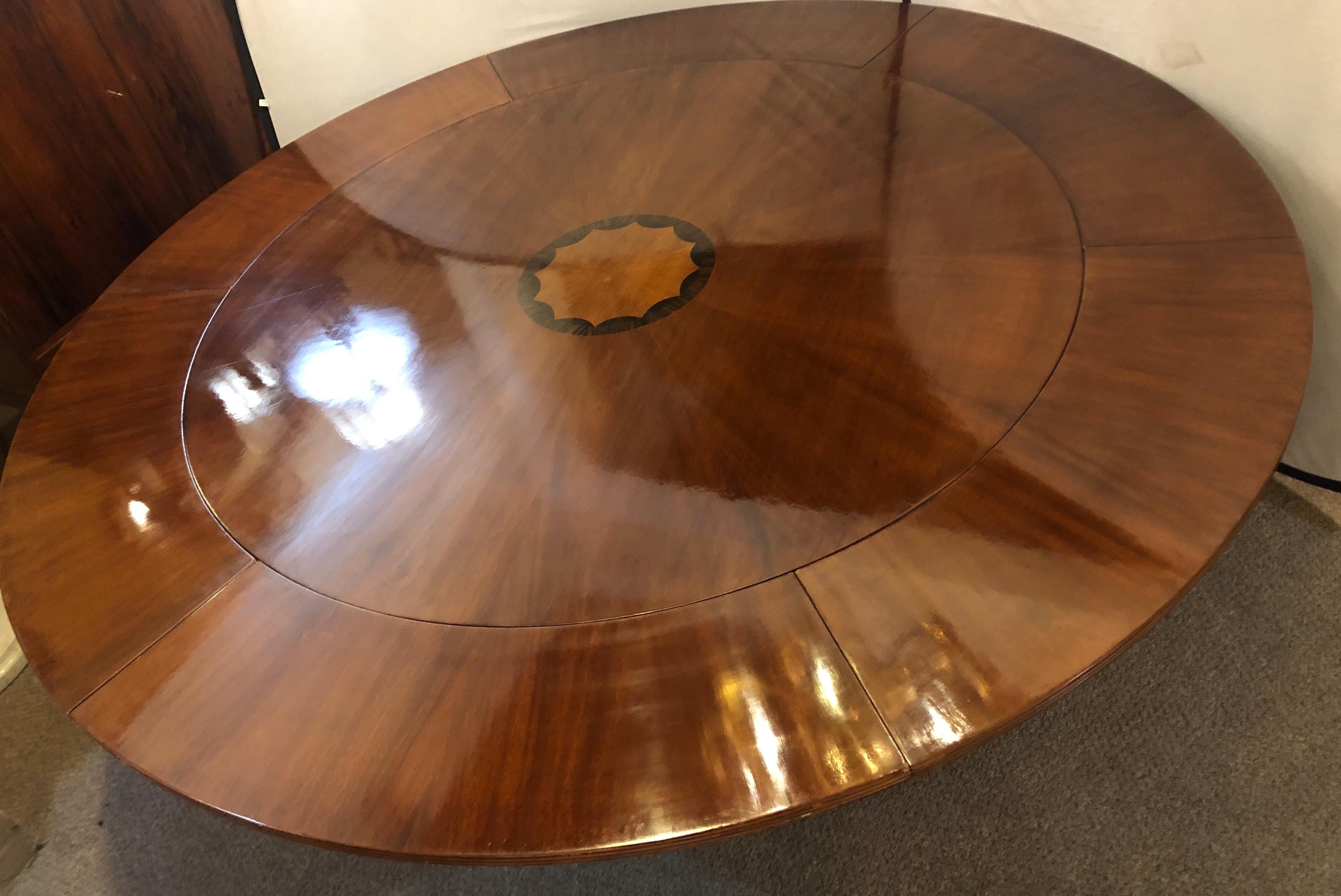 A John Stuart style circular inlaid expandable dining or center table. The sunburst table top sixty inches in diameter until it is fully extending with six leaves all measuring approximate 12 inches to an impressive 83.5 inches round. This table is