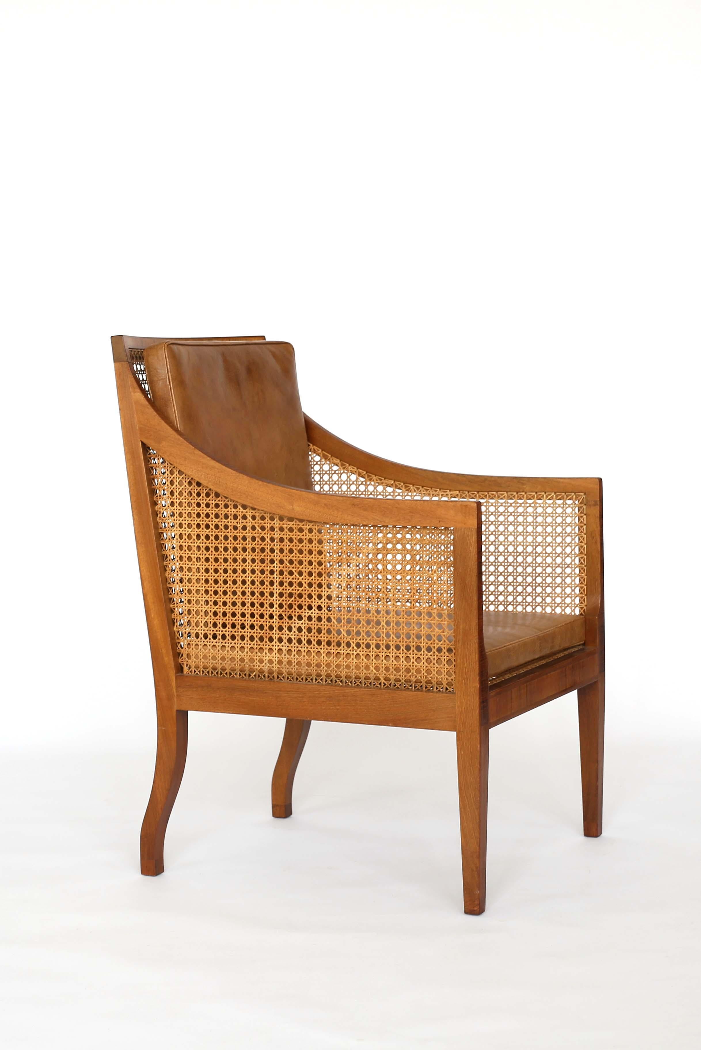 A Kaare Klint 'Bergere' chair. 

Mahogany frame with rosewood inlays and woven French-style cane, mounted with loose cushions upholstered with Niger leather. 

Designed by Kaare Klint, 1932 and manufactured by cabinetmaker Rudolf Rasmussen,