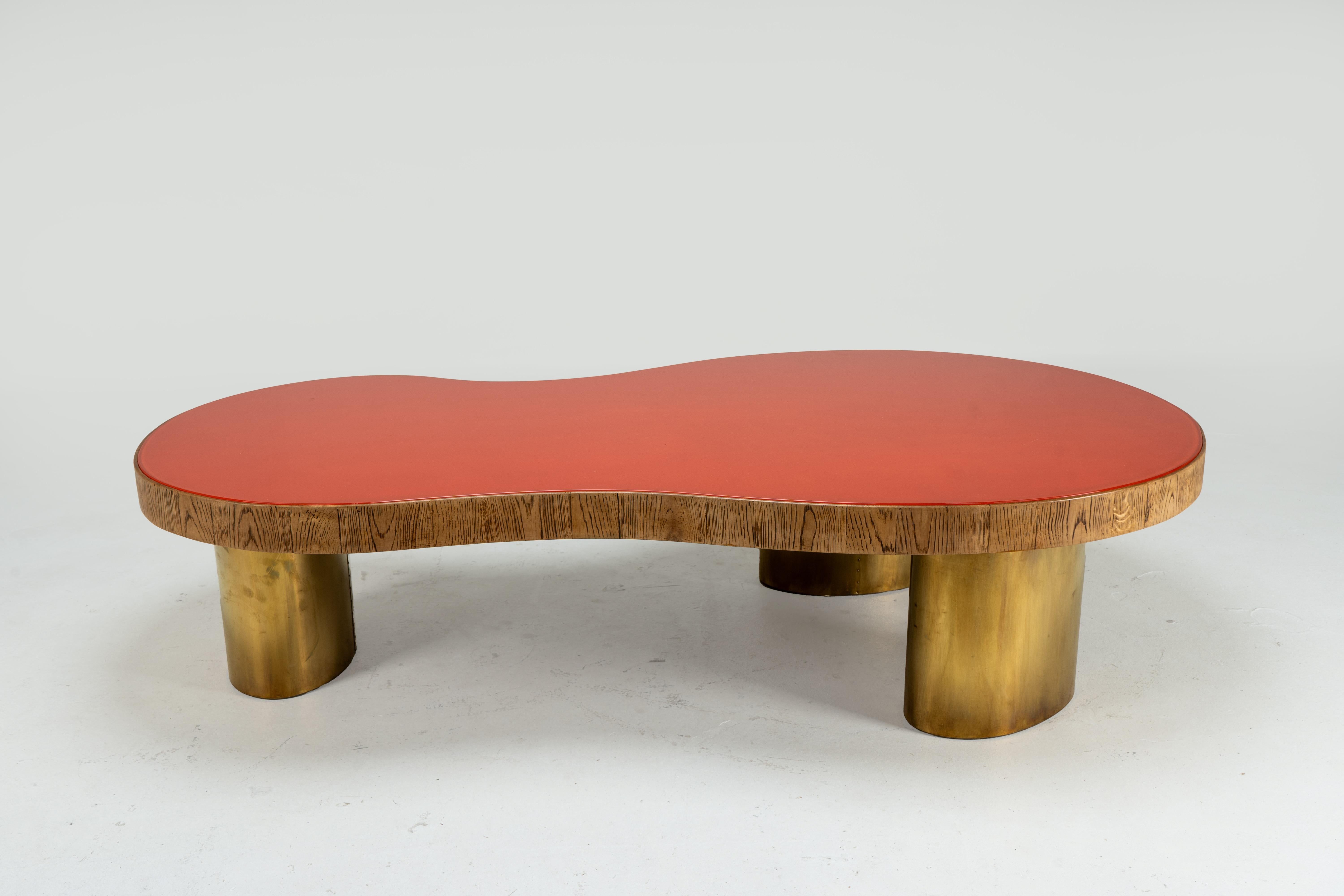 A rare kidney-shaped coffee table with a red glass top, cylindrical brass legs and walnut edge trim. The shape is inspired by the famous organically shaped coffee tables of French designer Jean Royère, who was known for mixing modernist elements