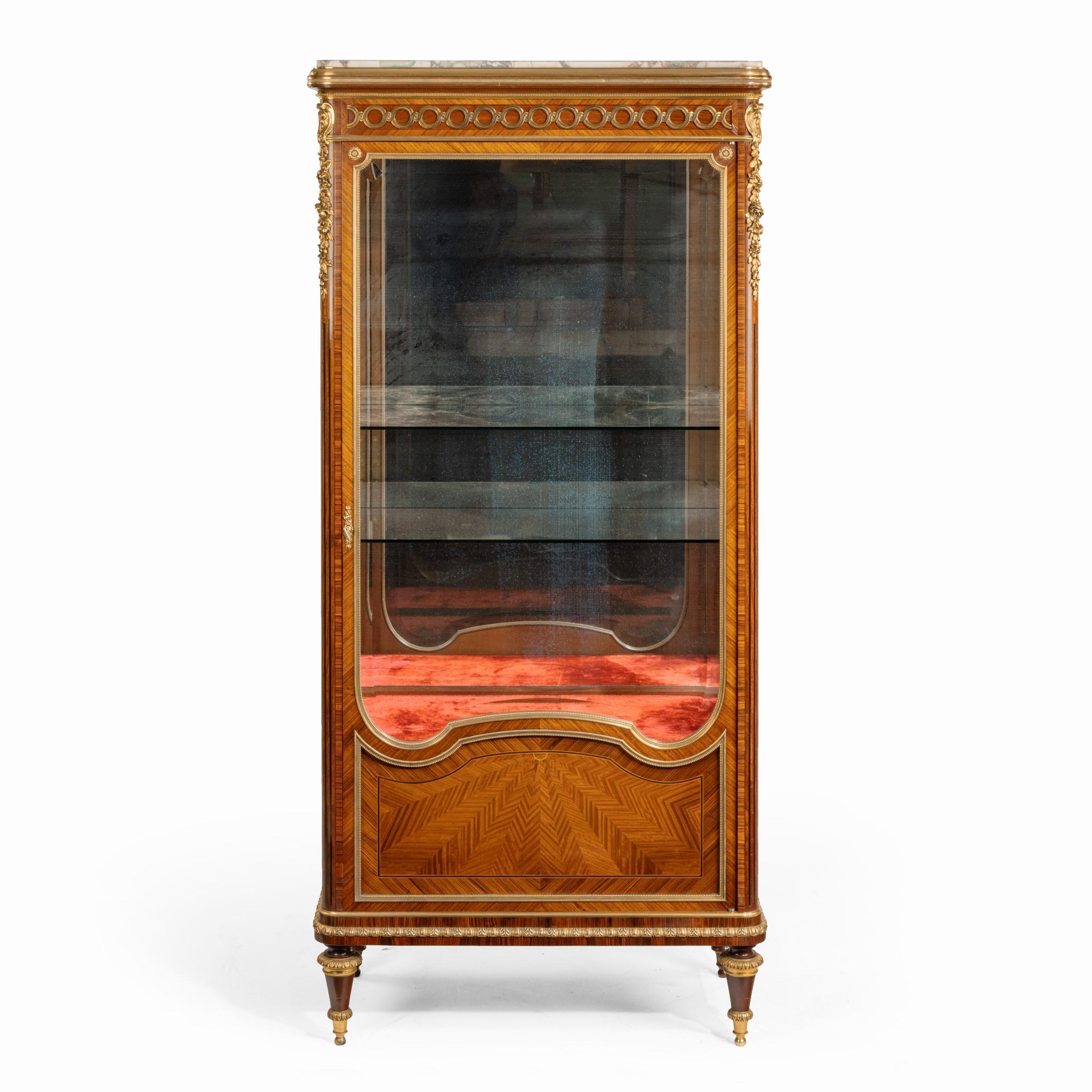 A kingwood display cabinet by Haentges Frères, of tall rectangular form, the single door three-quarters glazed above a shaped parquetry panel of radiating herring-bone cross-banding, enclosing a cupboard and two glass shelves, all raised on turned