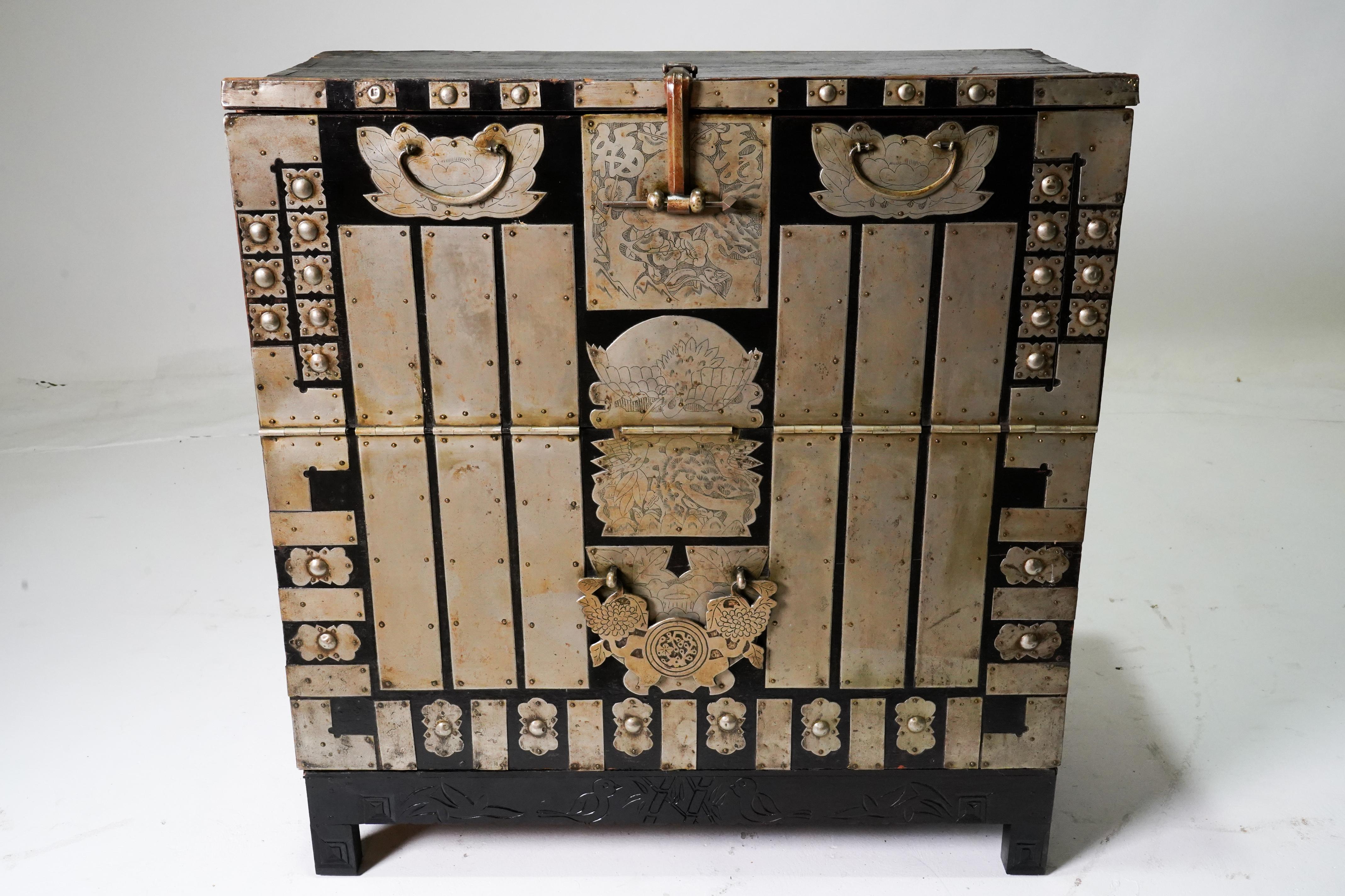 This brightly ornamented antique Korean chest once contained blankets and clothing given as part of a marriage dowry.  The distinctive feature of the piece is its abundant white brass hardware affixed to the solid elm wood body.  The piece has white