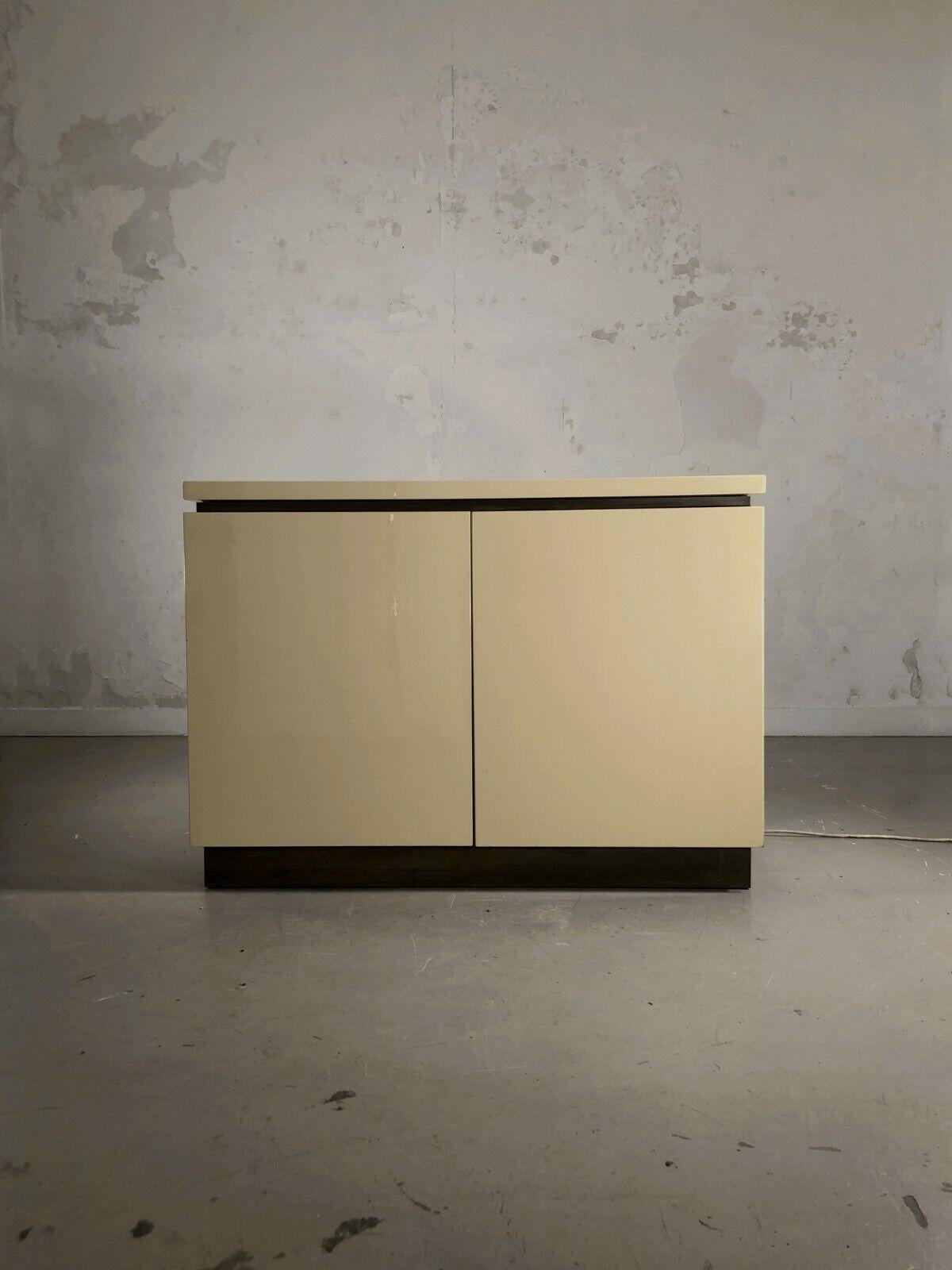 A minimal yet luxurious geometrical bar or buffet, Art Deco, Neoclassical, Shabby-Chic, in creme lacquered wood, finished with strips of golden brass or bronze, by Jean-Claude Mahey, France 1970. 
The buffet opens on the top in a way of a chest, to