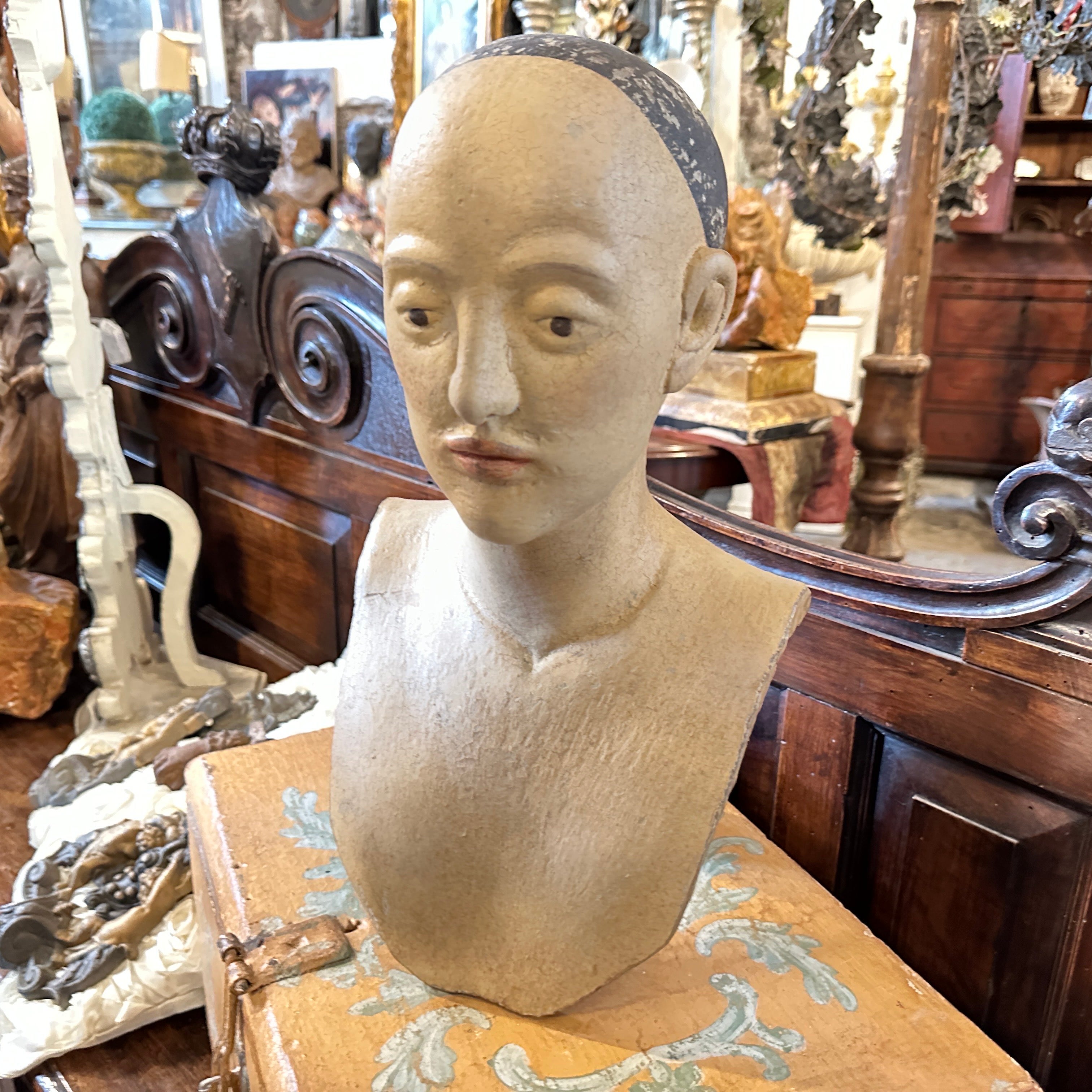 A lacquered wood bust that originates from Sicily, representing a stylized female figure. The bust is carved from wood and is finished with a lacquered painted surface, now worn with age. The woman has delicately carved features, arched eyebrows,