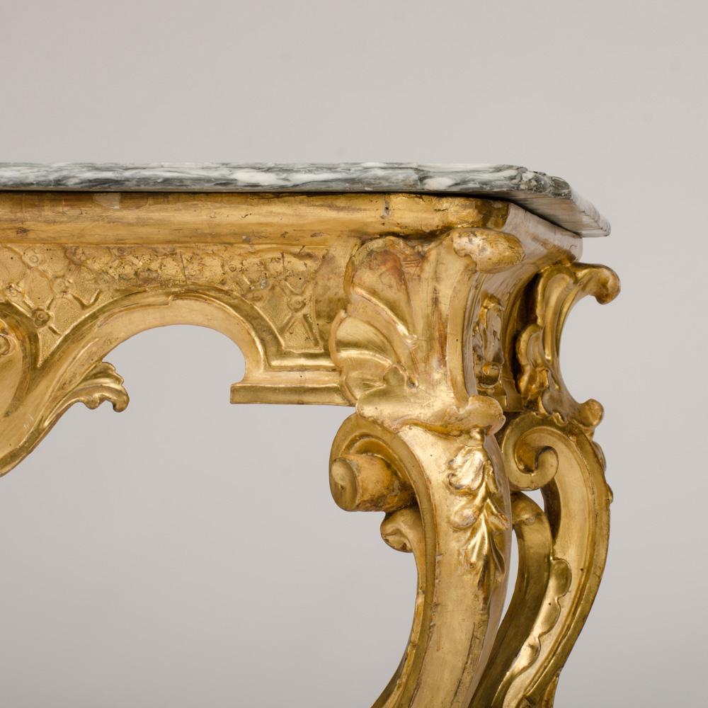 An Italian 18th c giltwood console table with original white and grey marble top. The frieze has a carved gilt wood shell, floral swags and is raised on cabriole legs united by a stretcher with flowers and shell decorations.