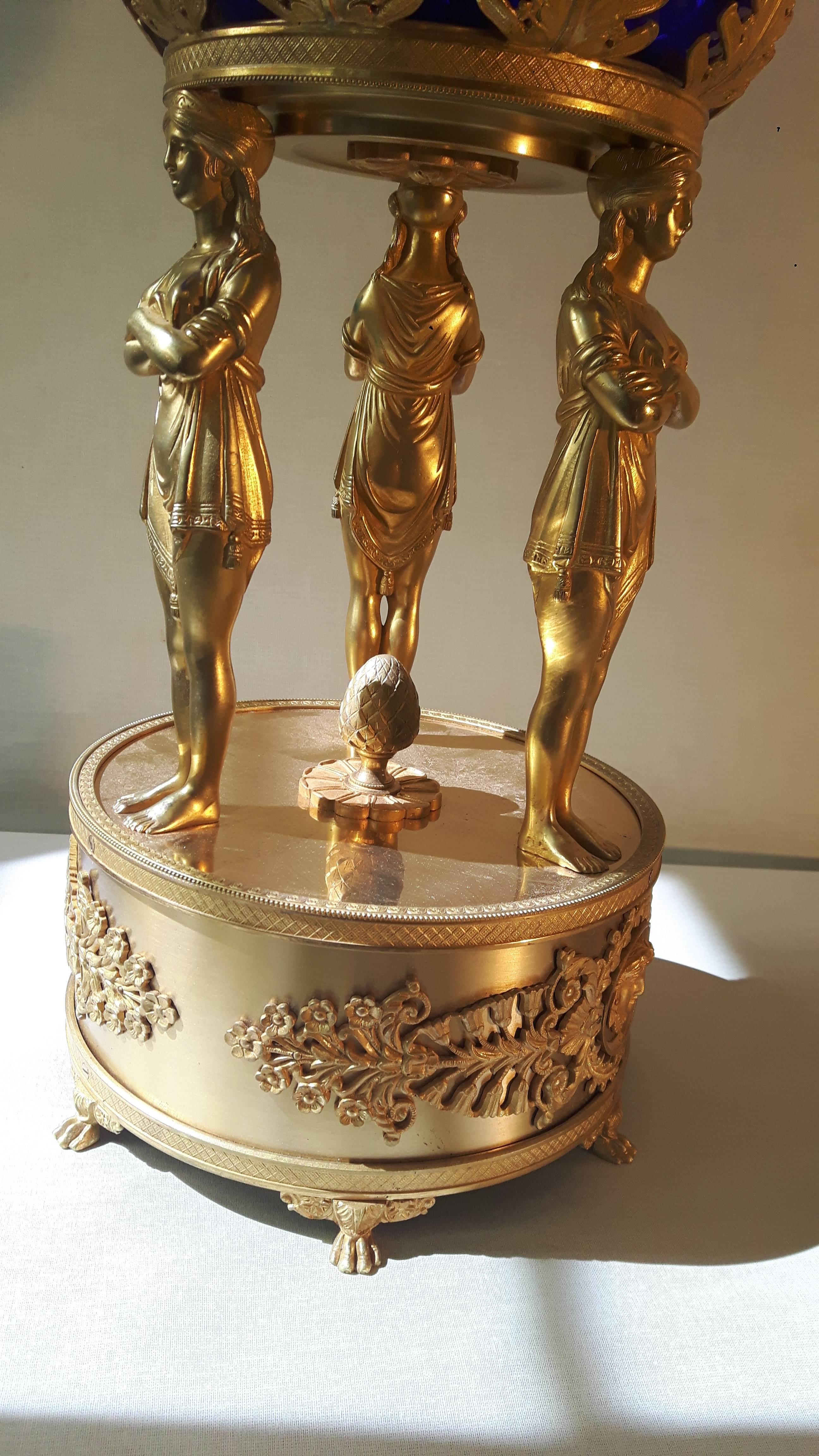 Spectaculaire tazza napoléonien, avec une coupe en verre bleu taillé au couteau entourée d'une couronne de feuilles d'acanthe en bronze doré, soutenue par trois vestales debout sur une base en bronze doré décorée de frises de style napoléonien et de