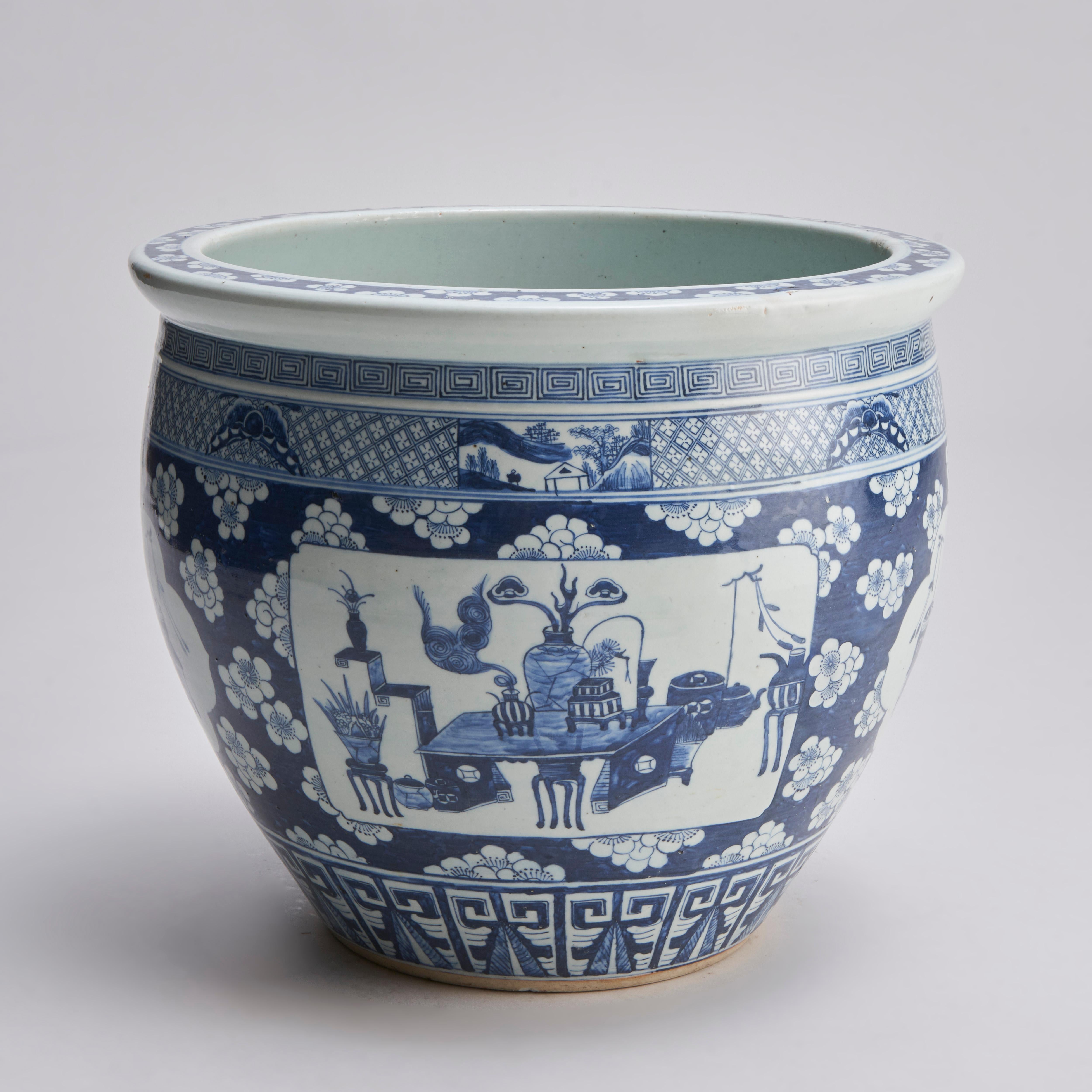 A large 19th century Chinese blue and white jardinere / fish bowl with dark blue decoration of panels of scholarly items and simple landscape scenes on a prunus ground with a meandering top border and a phoenix tail pattern to the foot.

The rim of