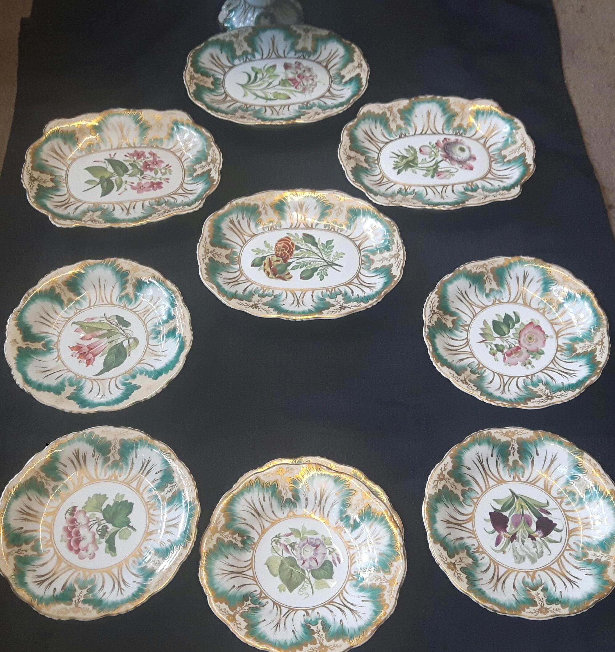 A Staffordshire porcelain botanical dessert service painted with flower
specimens inside green leaf and gilt borders, comprising: fourteen plates, four oval stands, four circular stands and a comport, impressed wreath and anchor mark, painted