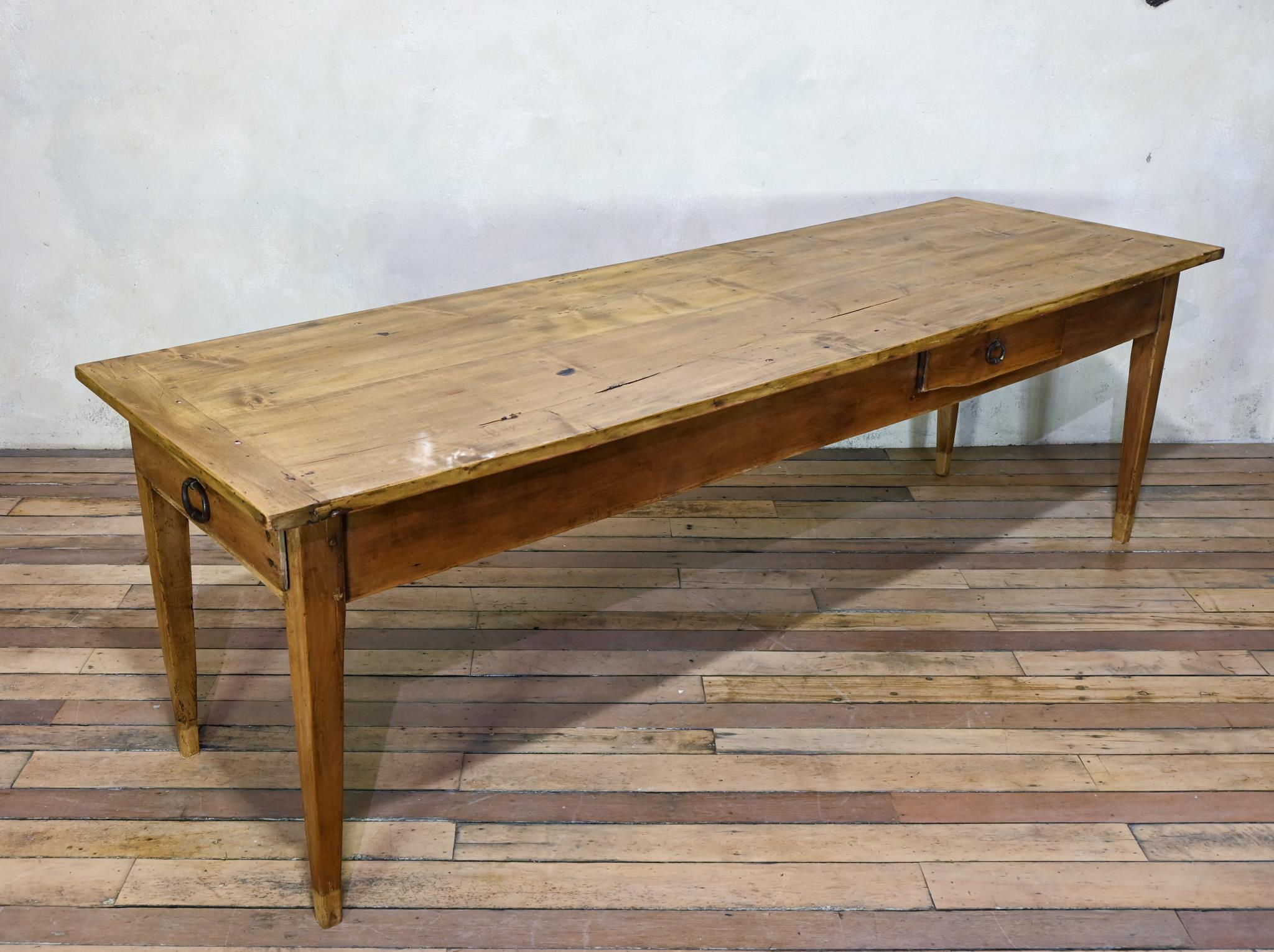 A 19th-century French farmhouse table constructed from fruitwood displaying a rustic charm. The spacious top features a gently worn surface, suitable for dining or various activities.
Supported by tapered legs, the table provides stability while