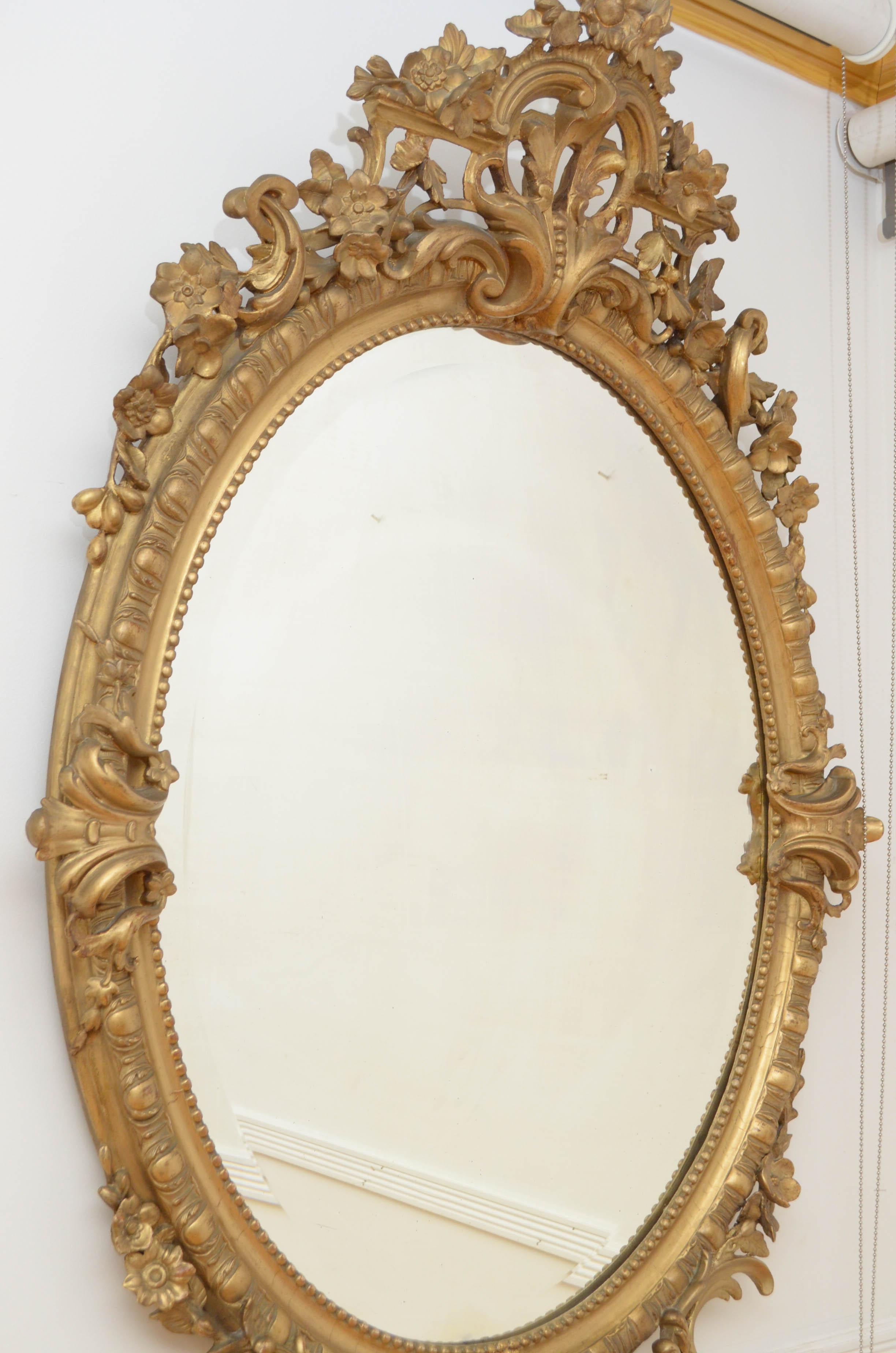 Sn4863 large 19th century wall mirror in giltwood, having original beveled edge glass with some imperfections in beaded and carved frame with extensive floral and shell decoration throughout. This antique mirror retains its original glass, original