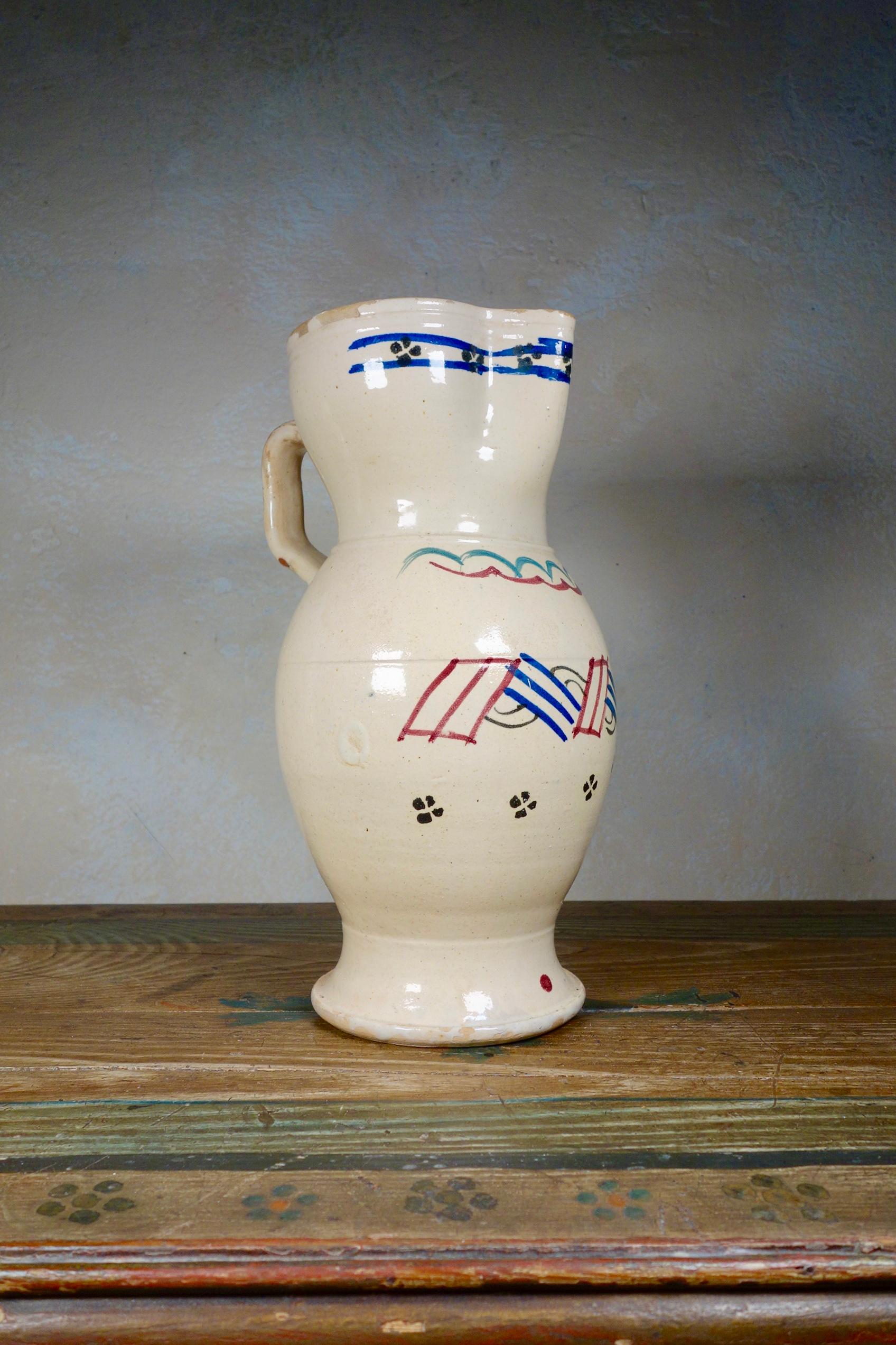 A large 19th century tin-glaze Pugliese Pitcher.
Featuring an elongated ovoid-shape body with a disc foot. The flat strap handle rises from just under the rim and ends just before the widest part of the lower body.
Painted with simple geometric