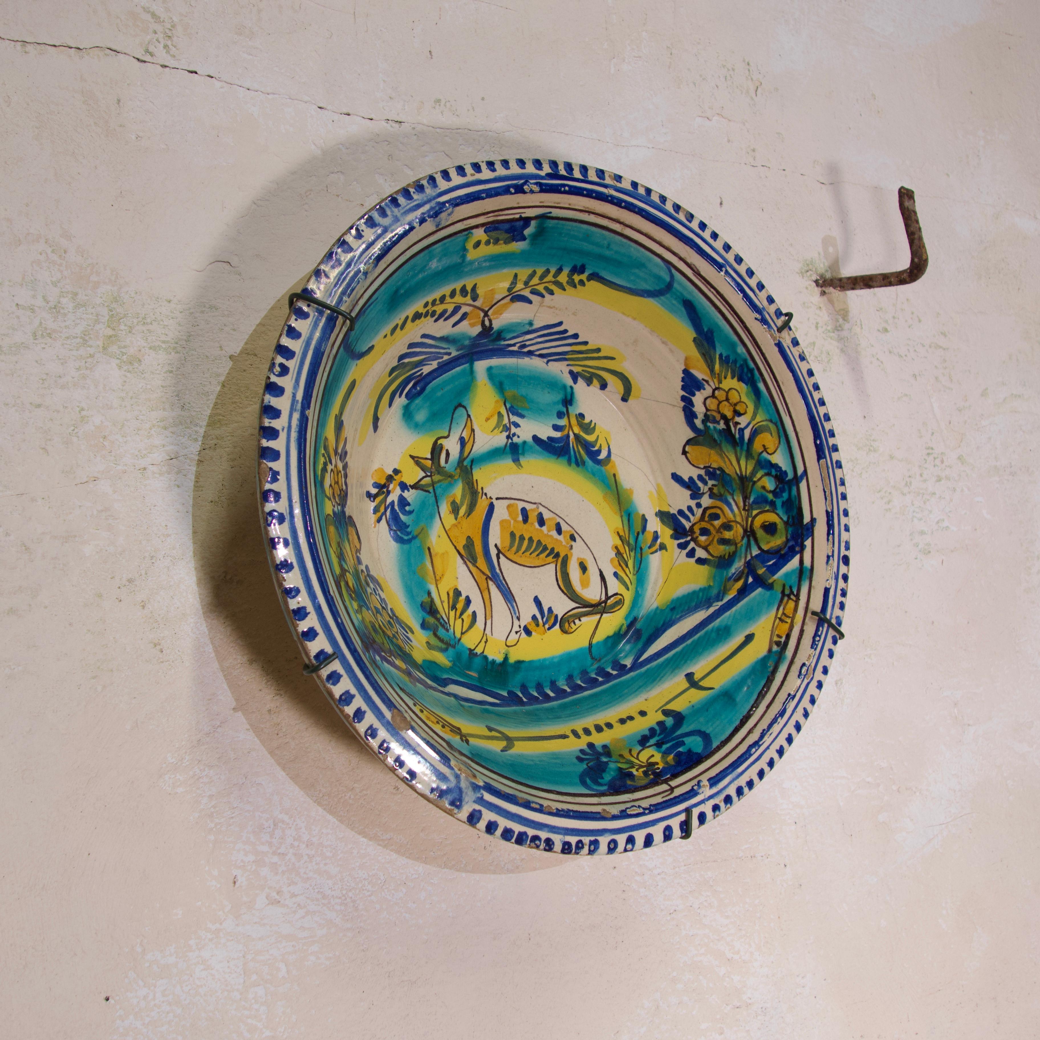 A large 19th century Spanish lebrillo from Triana. Of gently flared circular shape, painted in turquoise, blue and yellow with a central dog surrounded by flowers and foliage - the rim present with blue line and dash detailing.