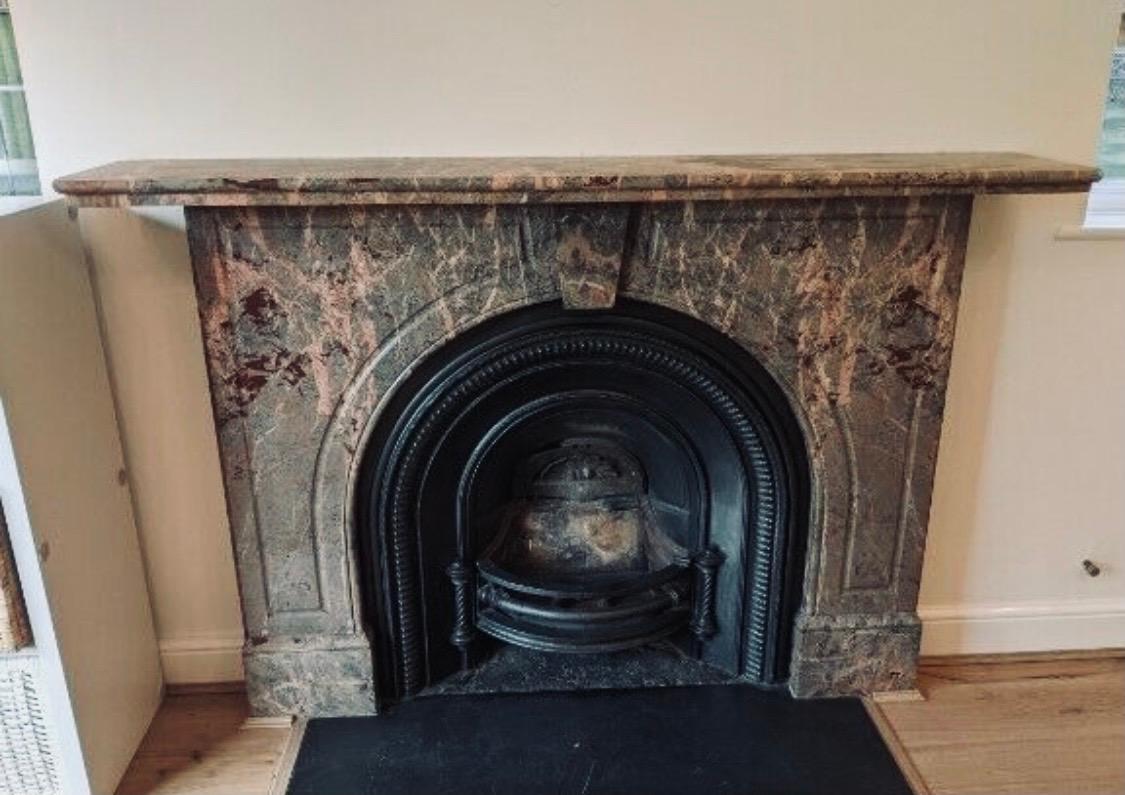 A large and versatile 19th Century Victorian arched spandrel fireplace surround carved in richly veined Rose en Jugerais marble. A generous double thick top shelf over an unadorned keystone, flanked by a pair of panel fluted arched book matched