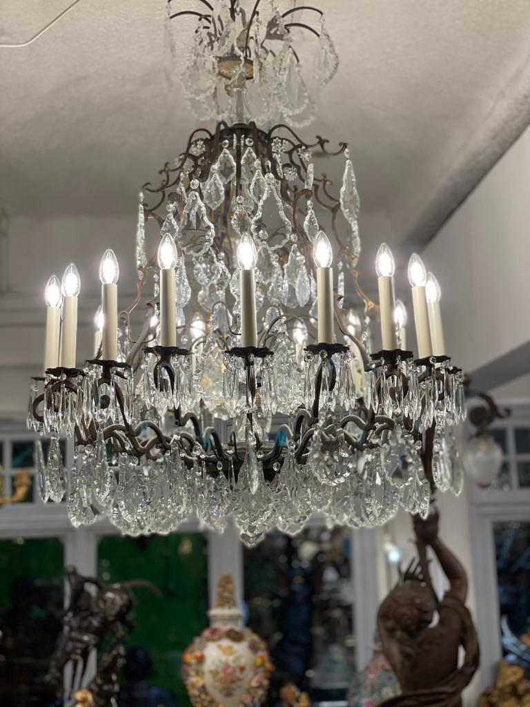 A large 20th century cut-crystal 18 arm chandelier in a patinated brass finish with a full complement of crystal droplets and a central cut glass stem. Metal birdcage type with large cut crystal pear drops.