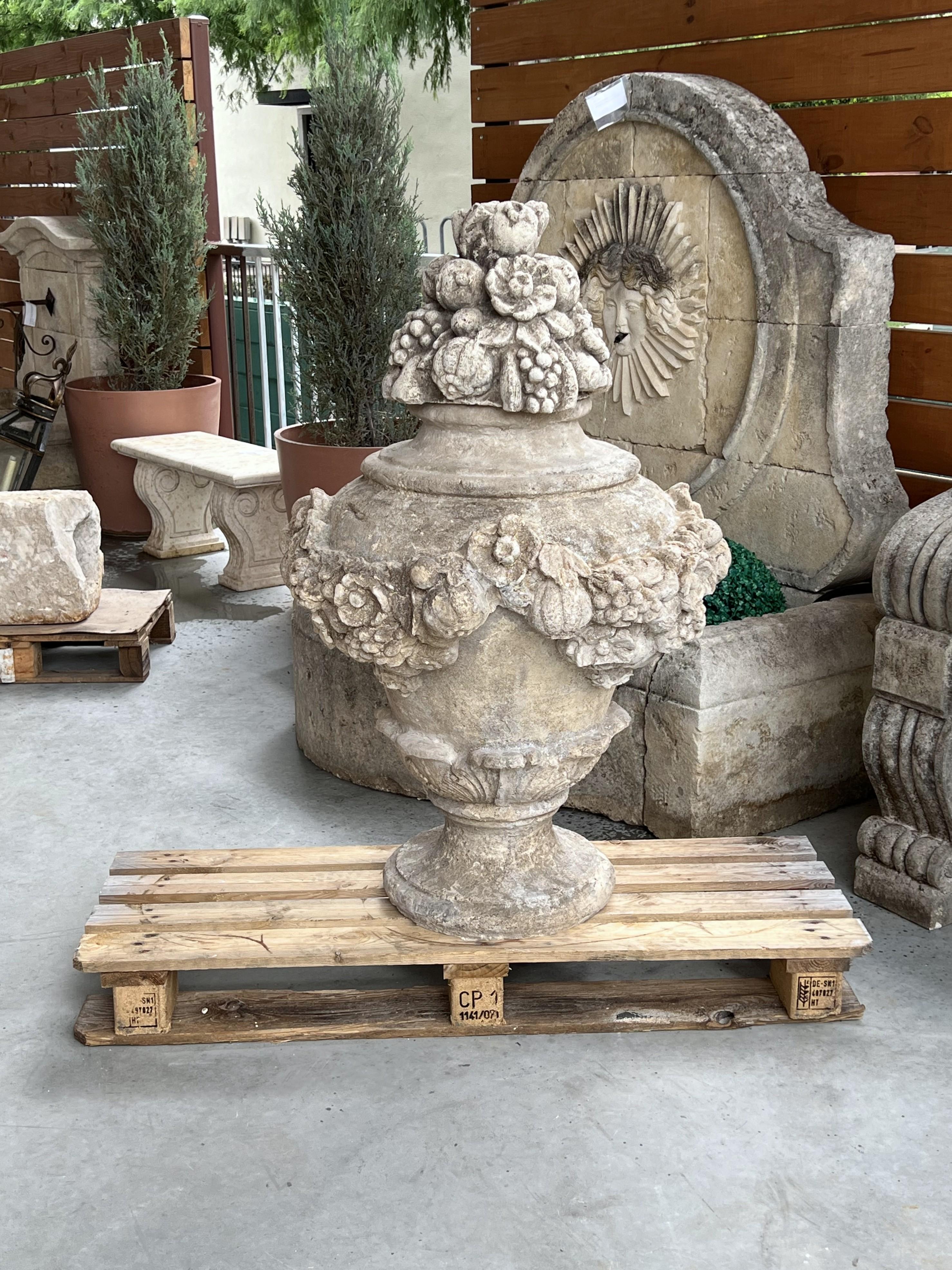 This large Italian fruit and floral urn would make an impressive garden ornament. Standing over 42 inches tall, the composite stone has a light gray hue with accents of cream, white, and dark gray. The billowing finial is comprised of a fruit