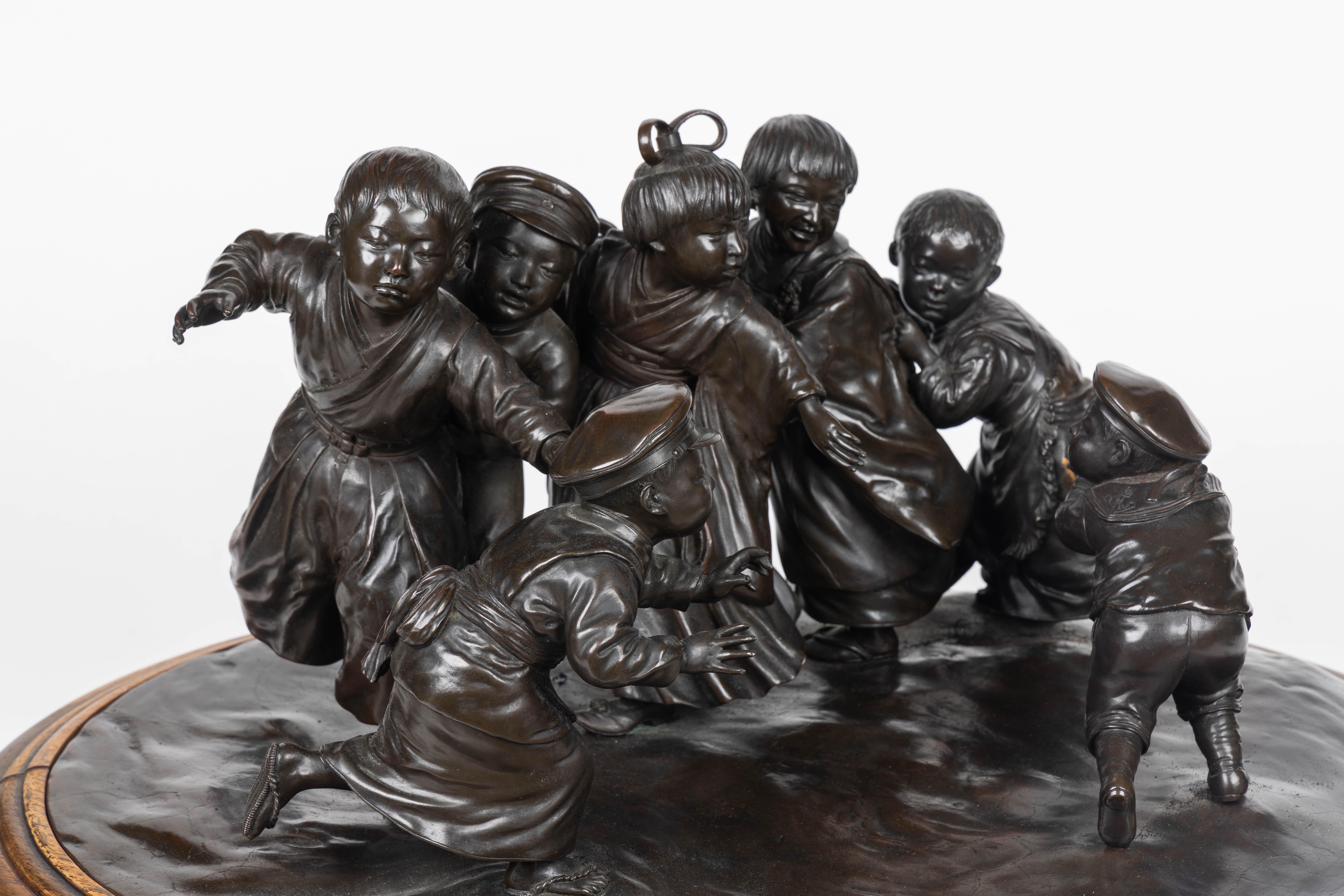 Wir präsentieren eine außerordentlich große und außergewöhnliche japanische Bronzeskulptur aus der Meiji-Periode der Tokioter Schule, die ein entzückendes Ensemble von sechs energischen Jungen darstellt, die ein einzelnes verspieltes Mädchen beherzt