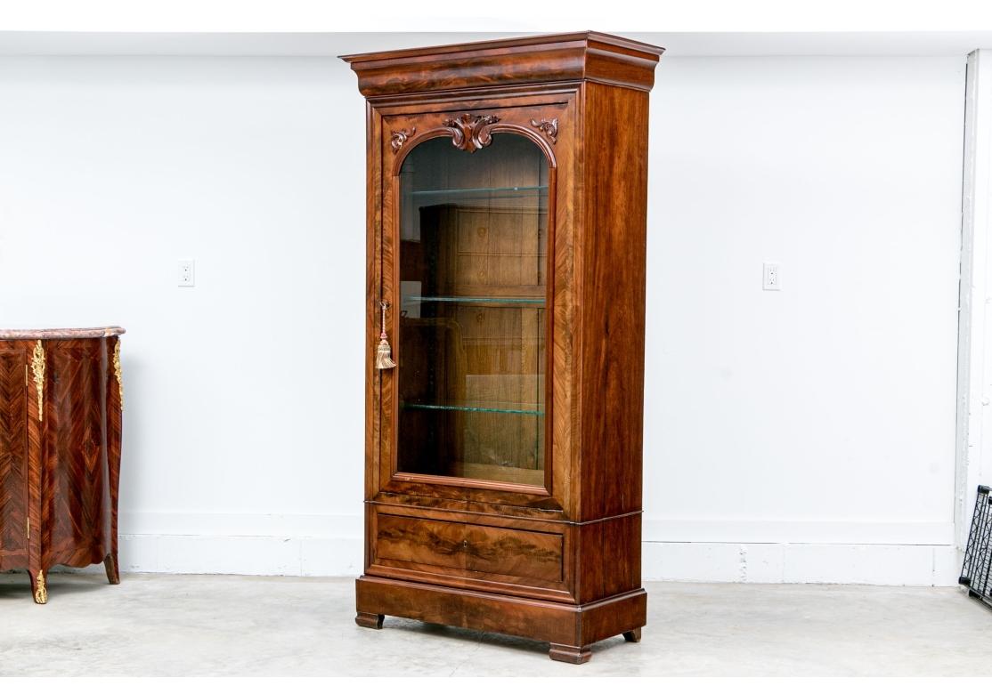 Una refinada vitrina o librería antigua de finas proporciones y gran veteado de madera. Con una puerta de cristal con llave de trabajo que se abre a una trasera con paneles de roble y tres estantes de cristal ajustables con listones de madera de