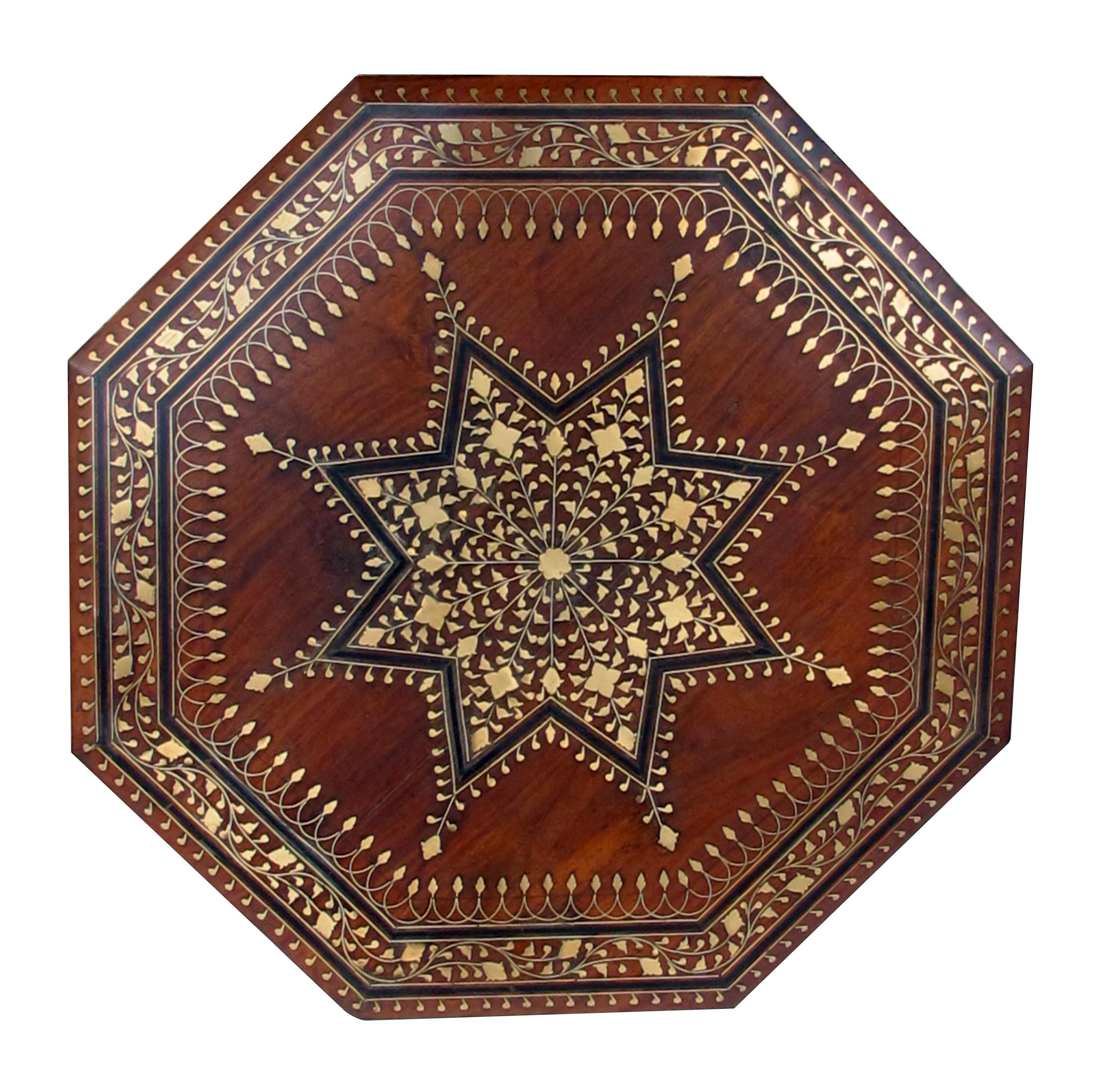 Originally used as traveling tea tables for the British in India; the octagonal top with central star medallion surrounded by meandering foliate vines; raised on a conforming hinged openwork base.