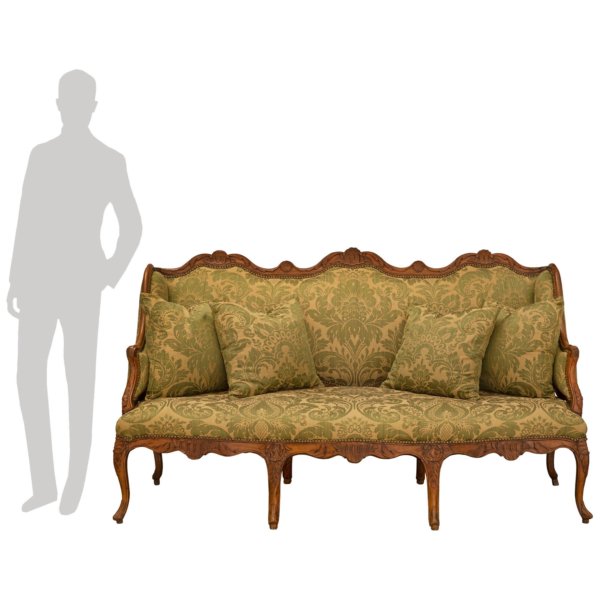 Un sensationnel canapé en noyer de style Louis XV du début du 19e siècle. Huit impressionnants pieds cabriolets à volutes et à sculptures florales soutiennent ce meuble. Chaque pièce est centrée d'un motif de feuille d'acanthe sculpté. Au-dessus se