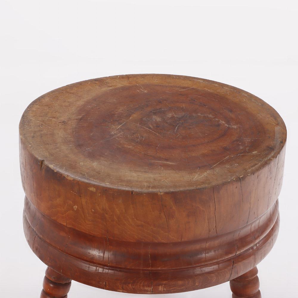 Une grande table ancienne en bois de boucherie avec un plateau circulaire naturel reposant sur des pieds tournés.