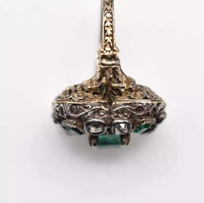 Antique, foreign silver set on unmarked yellow gold, emerald and diamond large rectangular cluster ring. With a single, centre-raised, rectangular mixed cut emerald approximately 6mm x 4.8mm with four corner emeralds 2.5mm x 1.75mm each, interset