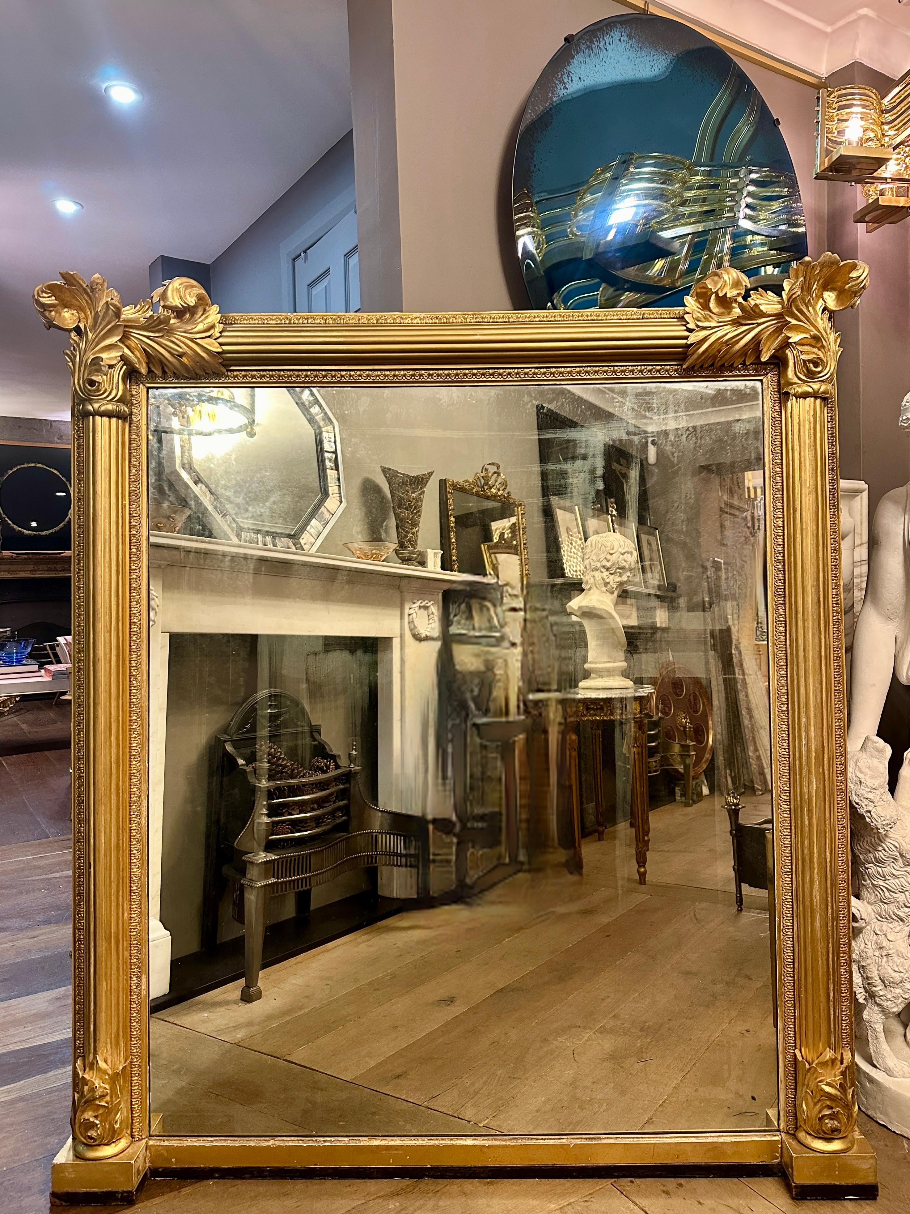 A large gilt wood English Regency period over mantle mirror. The frame with reeded columns decorated with large carved acanthus to top and bottom. retaining its original silvered mirror plate, with foxing as shown in images. The  back panelled. A