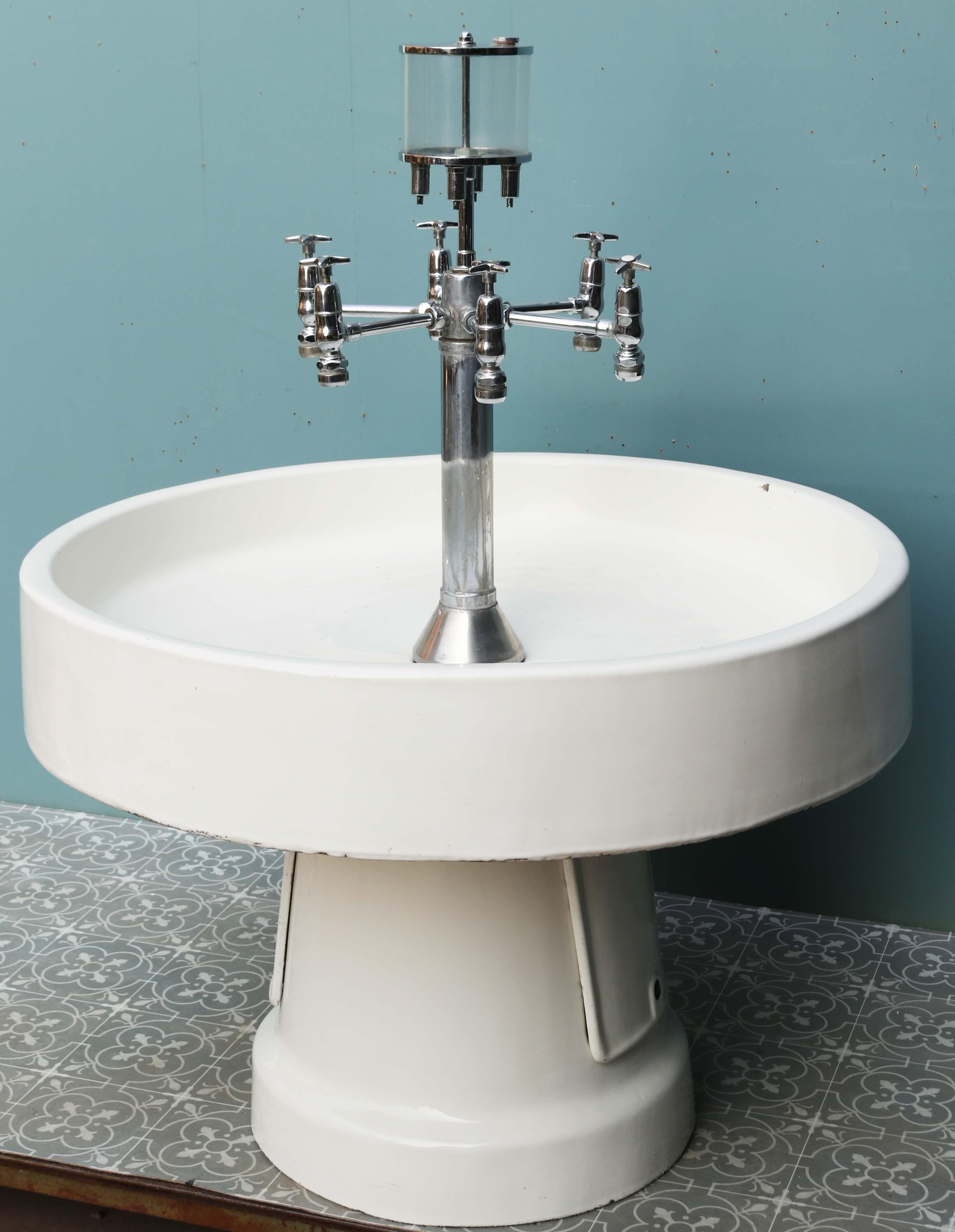 A large Antique freestanding circular sink. An impressive six tap, communal washing station. The sink features an acrylic multi use soap dispenser and is likely to be manufactured by Doulton and Co. We have another matching sink available. This