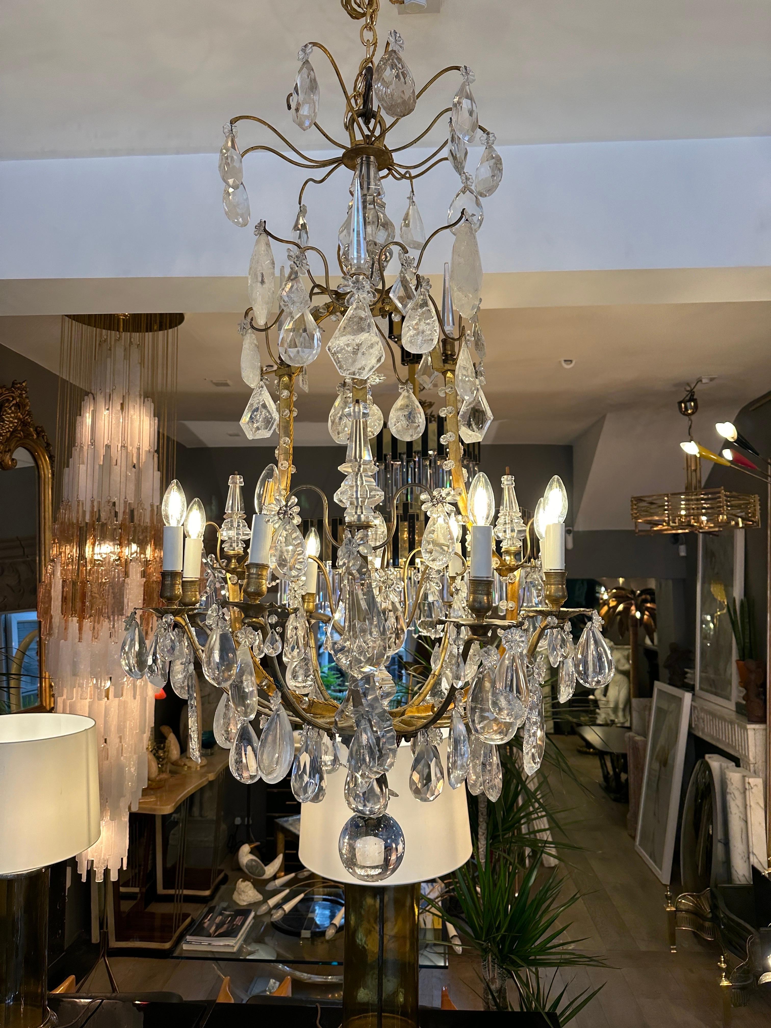 A large gilt bronze cage frame rock crystal chandelier from the late 19th century. Embellished with rock crystal and cut crystal pieces, The caged frame decorated with beads and flowers. 10 candle bulbed arms with alternate drip pans in bronze,