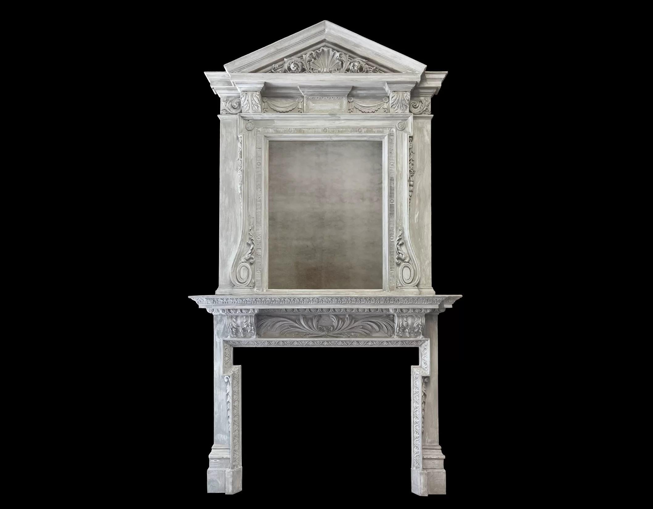 A large antique painted wooden fireplace with overmantel mirror.
Made in the George II Palladian taste and retaining its original painted finish.

The bottom section frieze with a laurel spray flanked by bracket corbels, this above a dog legged