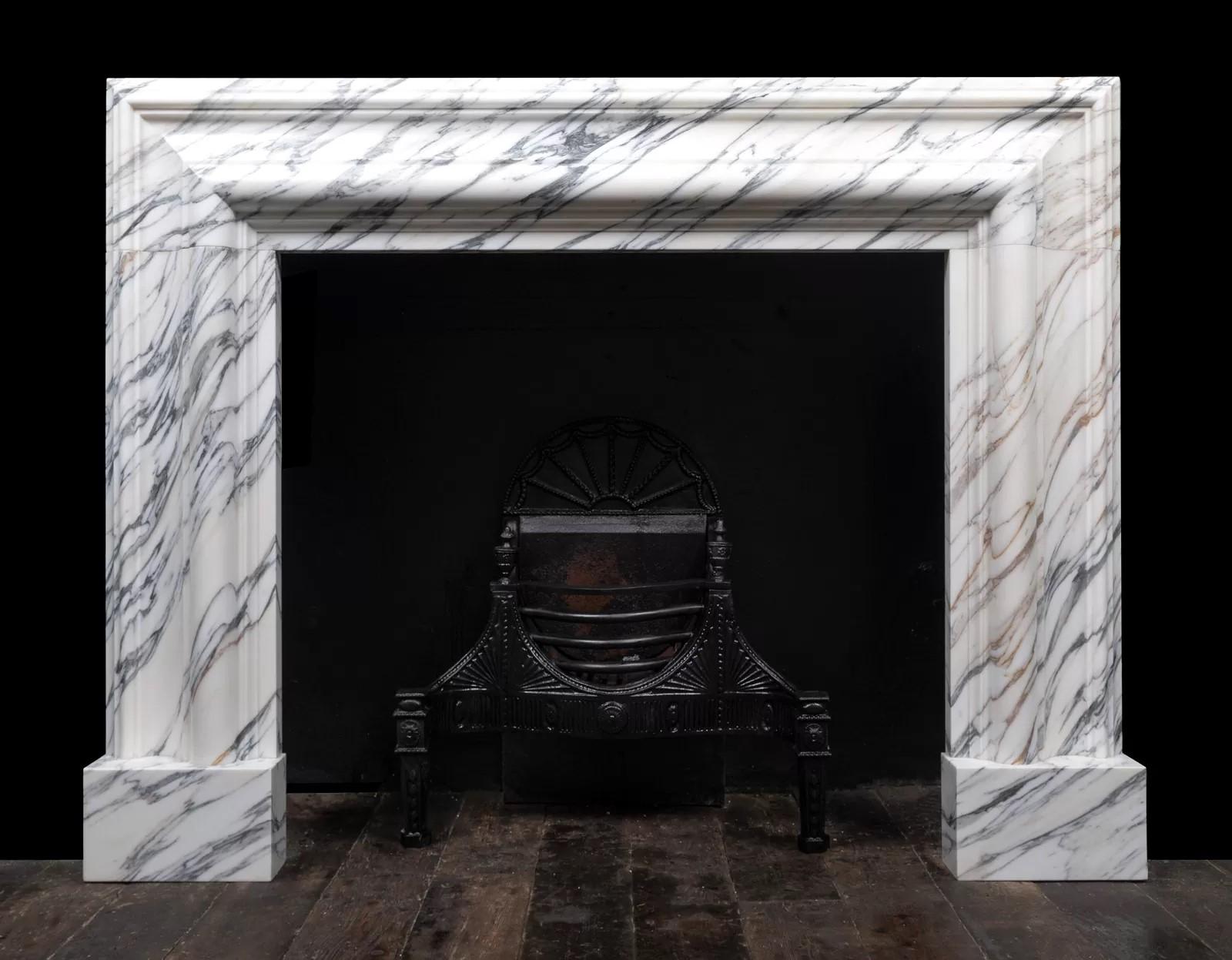 A large bolection fireplace surround of generous proportions by Ryan and Smith.

The substantial 12″ (300mm) wide bolection moulded frame, rests on plain square plinths.
Carved from a block of beautifully figured, Italian Arabescato Carrara marble,