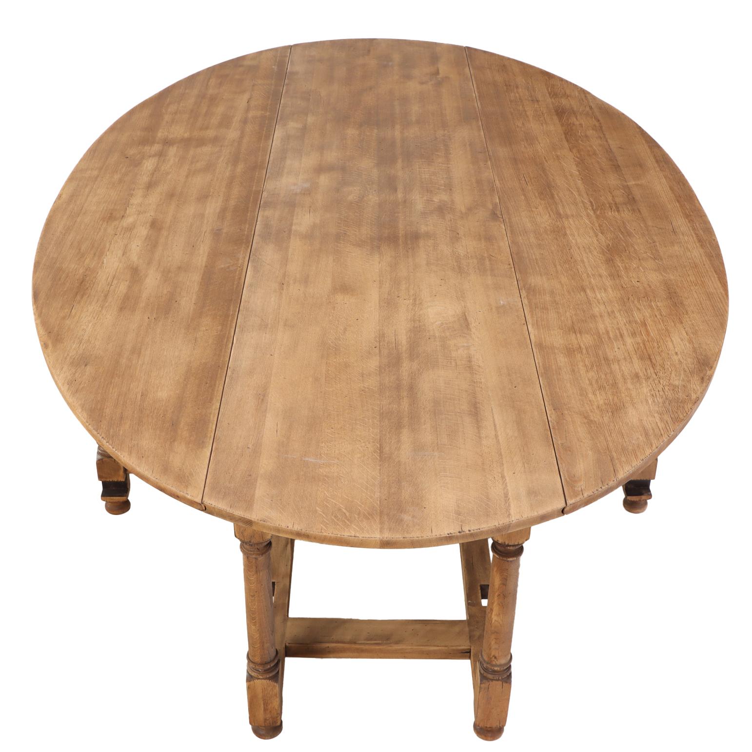 Une table à pieds en chêne belge, substantielle et bien fabriquée, avec un plateau ovale classique et deux portes-fenêtres. La vaste surface est soutenue par une base composée de pieds en balustre tournés, avec quatre supports de pieds de porte qui