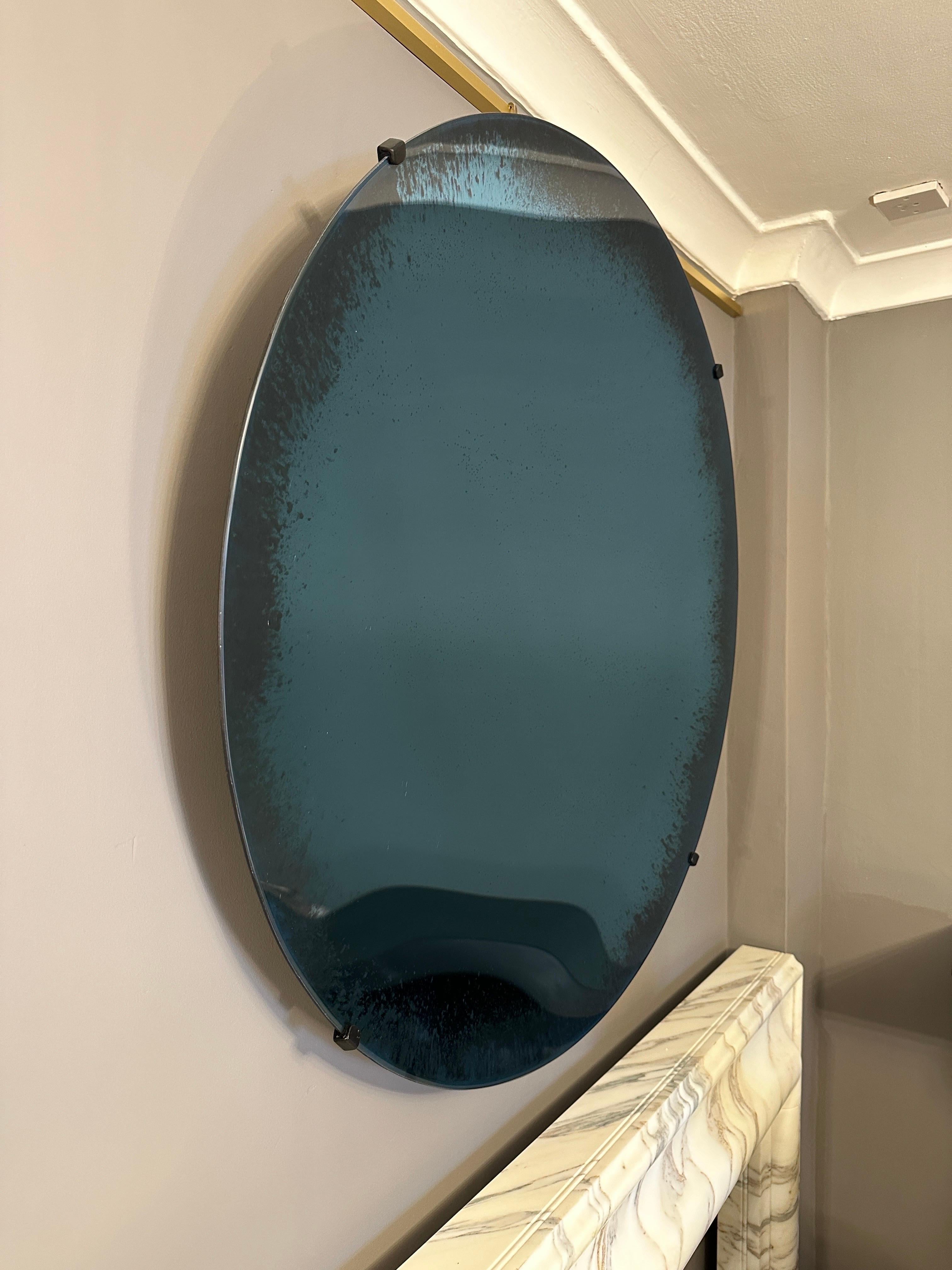 Un grand miroir concave en bleu avec un bord extérieur en relief. Heldly par des clips en acier noir. Les images sur le curseur présentent des reflets et une profondeur de couleur. Un miroir de bonne qualité avec de belles couleurs et une grande