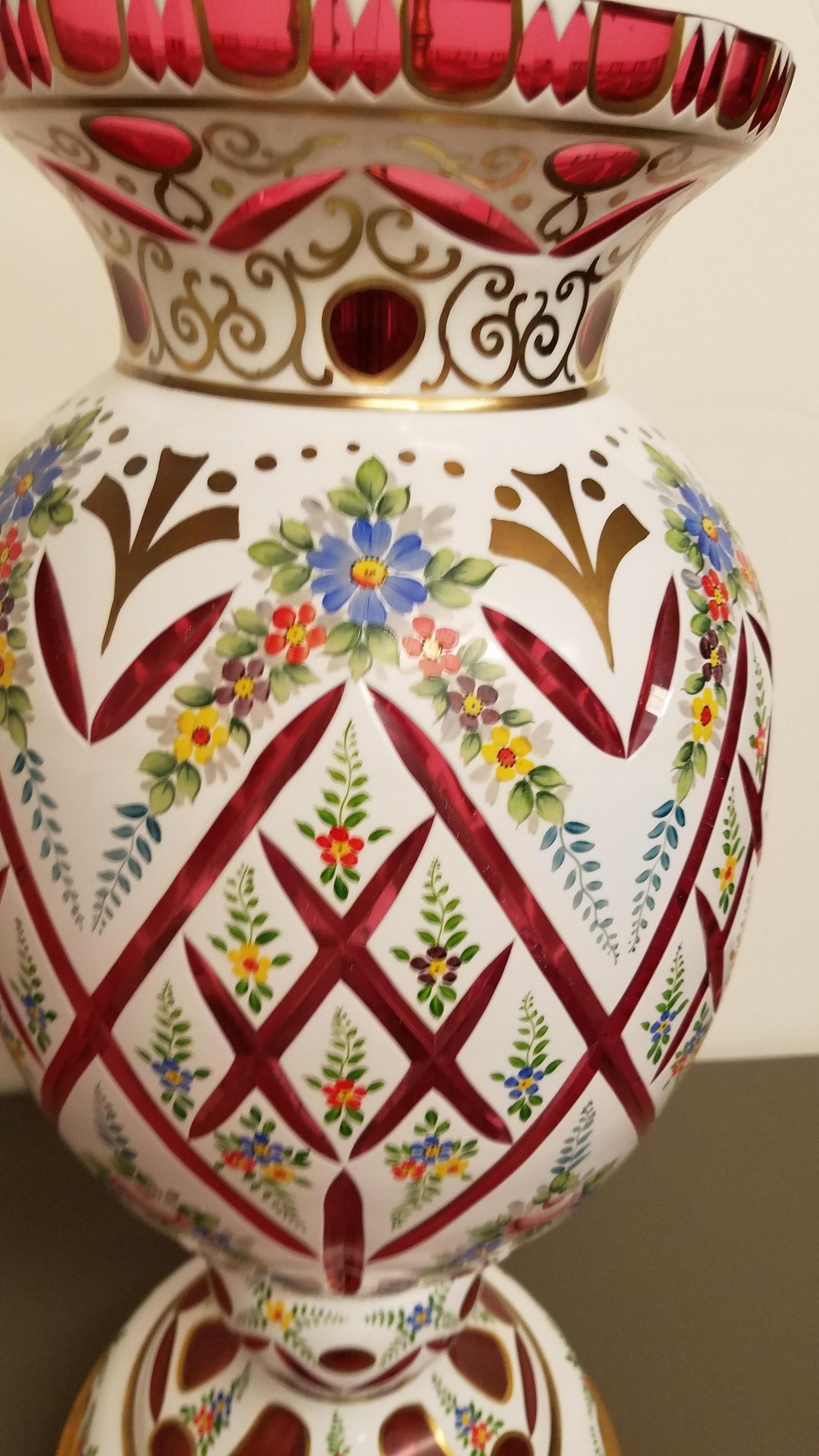 A large ruby cut Bohemian and white glass hand painted urn lamp. The cased glass vase with delicate hand enameled floral decoration with spaced cuts between he hand details. The lamp to the top of the socket is 27.5 inched tall and with an